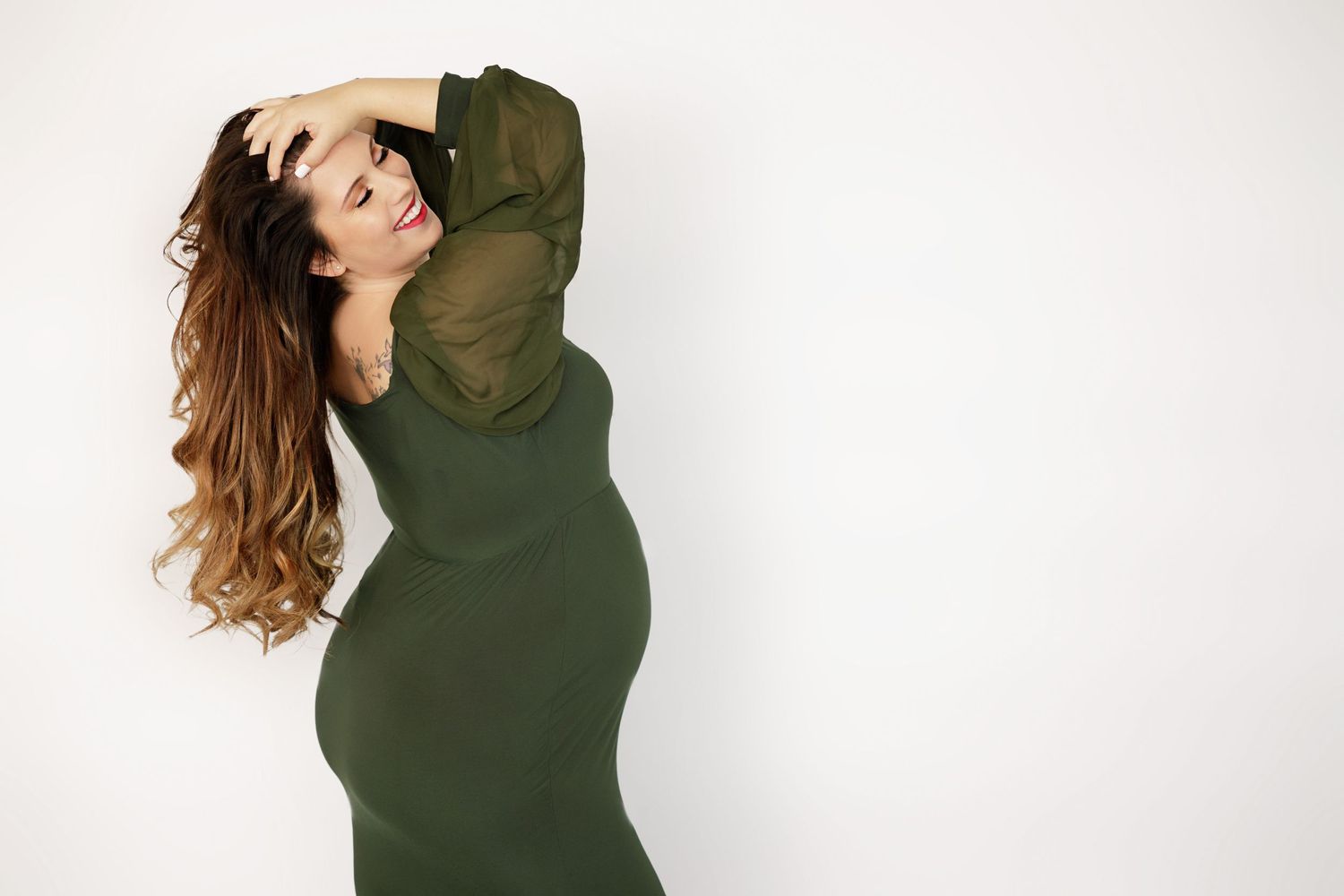 Woman in olive green dress poses against white background showing off flowing hair.