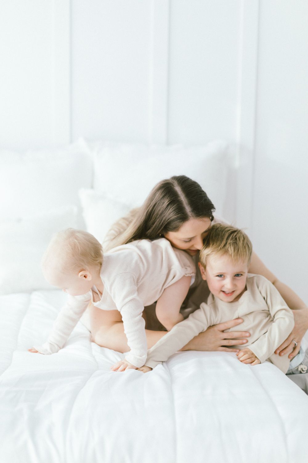 Family enjoying playful moments together while lounging on white bedding.