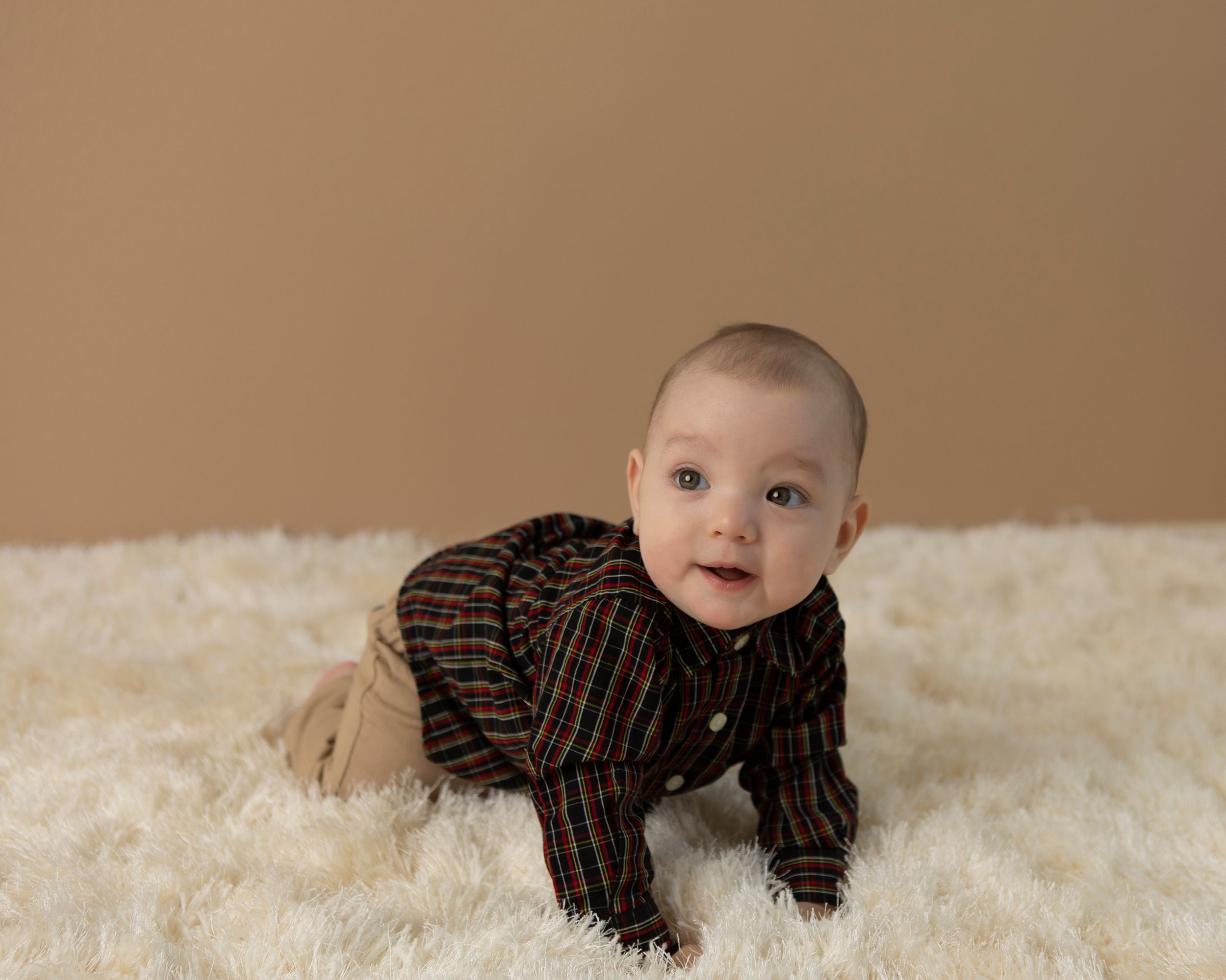 Infant wearing striped outfit crawling and smiling on white shag rug.