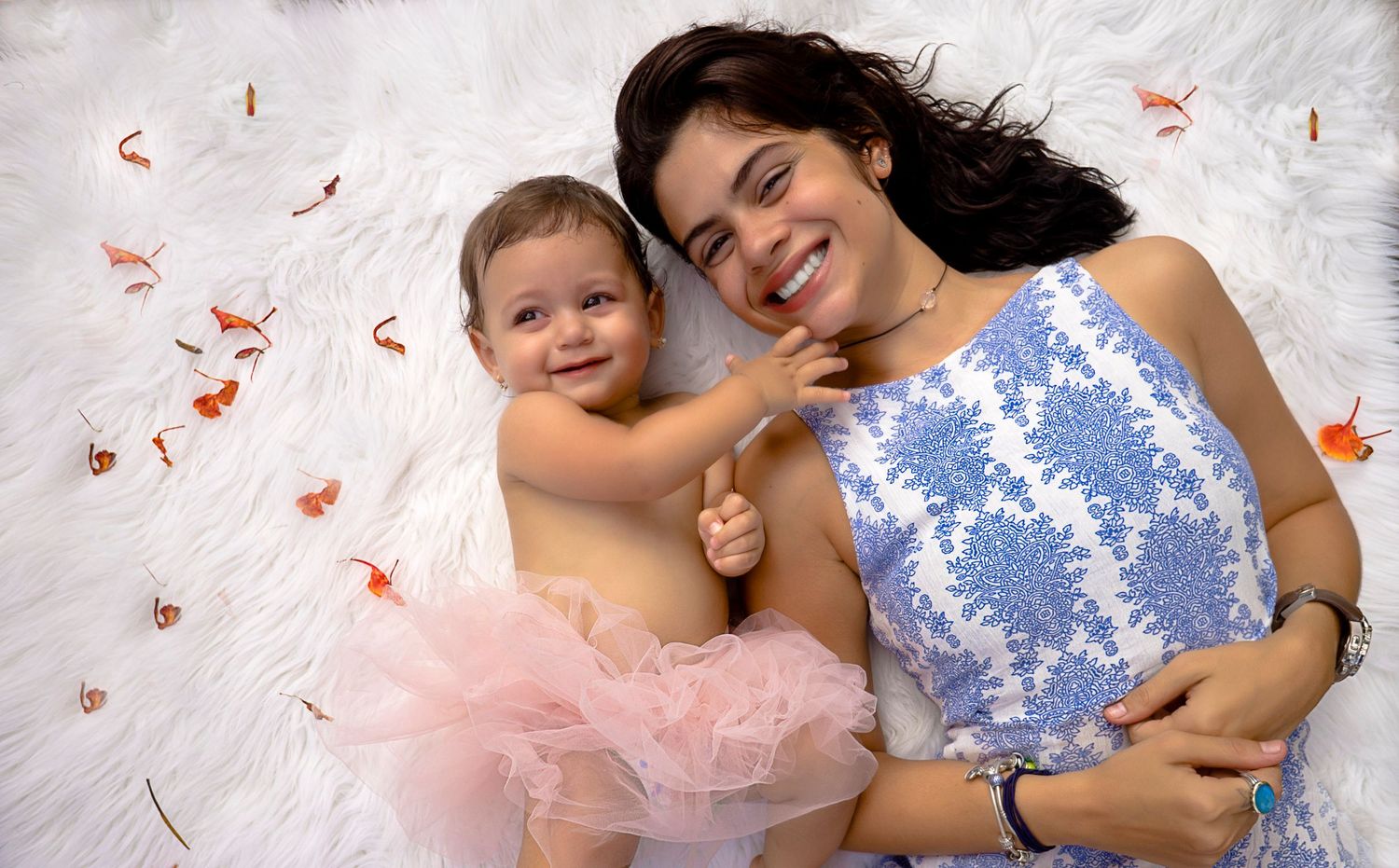 Baby in pink tutu laying on white surface with confetti and floral decorations.