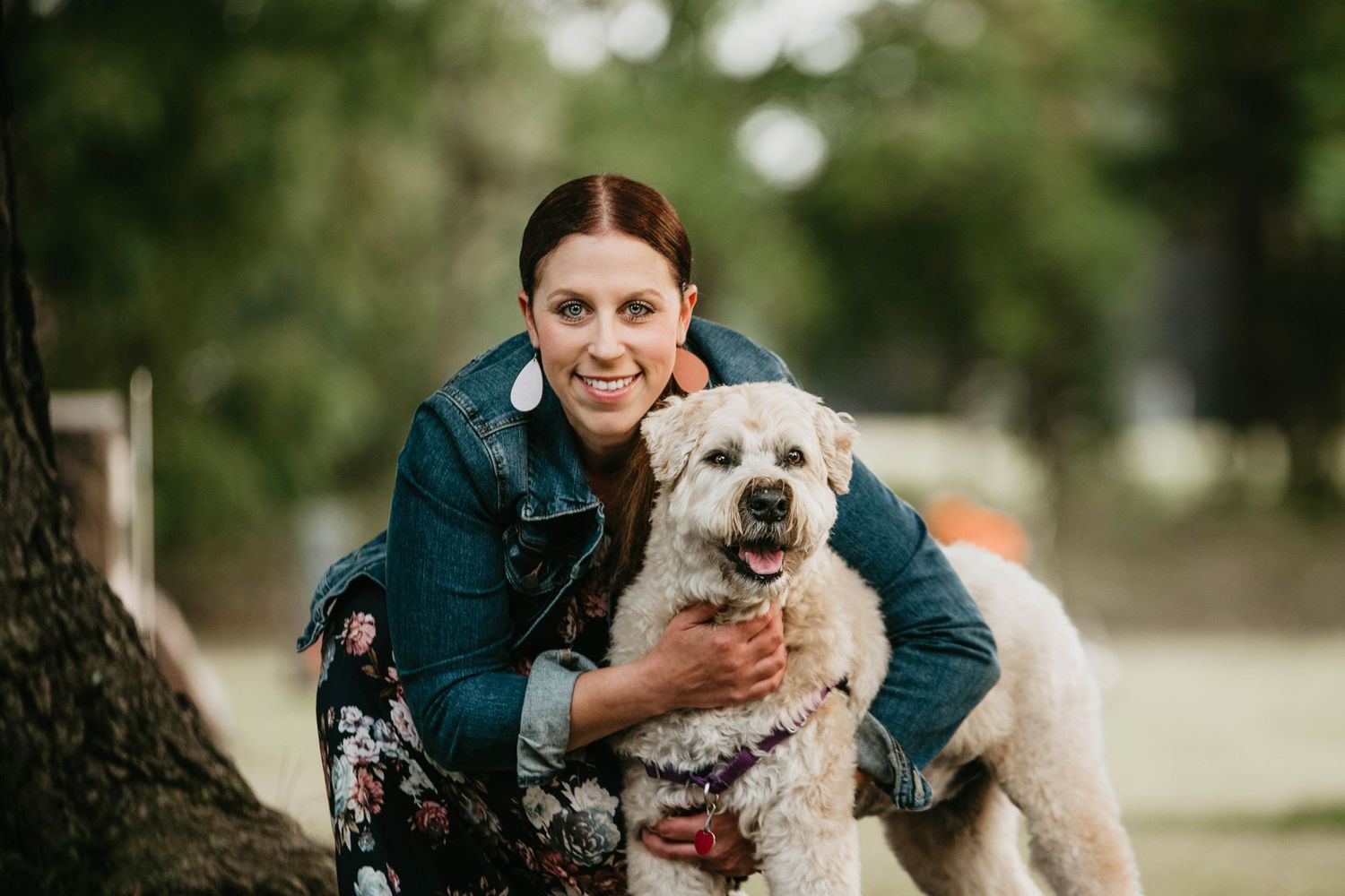 A fluffy white dog with curly fur plays outdoors with its owner wearing a teal jacket.