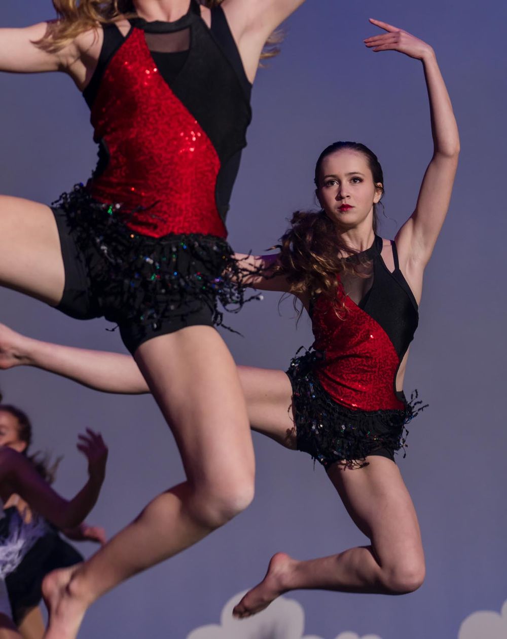 Dancers in red and black costumes perform synchronized jump during dance routine.