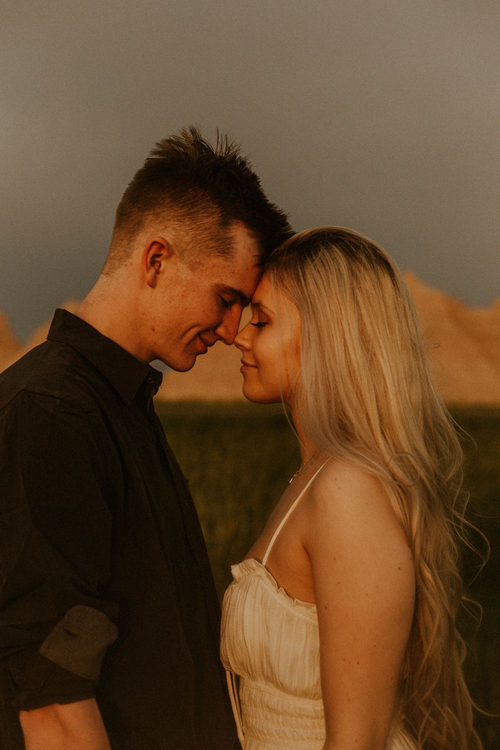 Engagement session in Badlands National Park. Couple rests heads together during sunset.