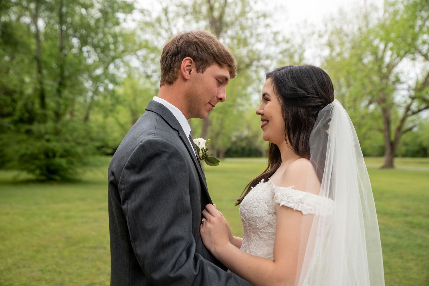 A couple shares a joyful moment together on their wedding day in a lush green outdoor setting.