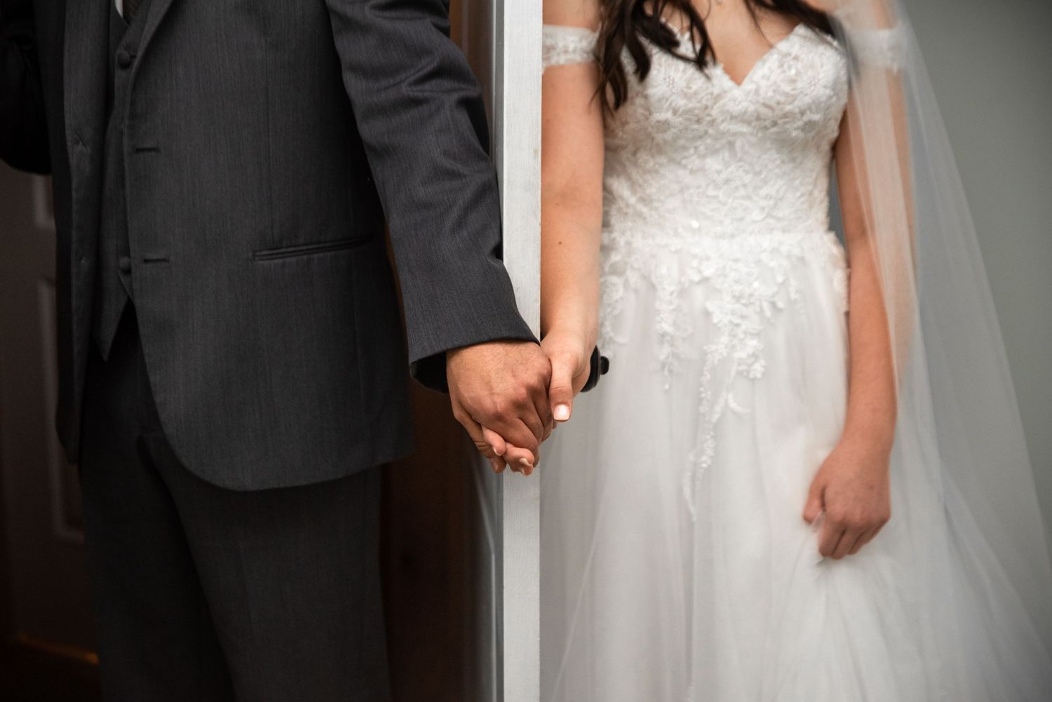A close-up shot of newlyweds holding hands, with the bride wearing a white lace gown and the groom in a dark suit.