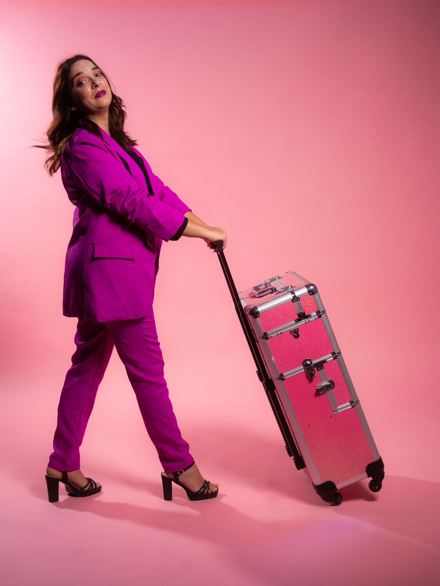 Dynamic poses with pink luggage against vibrant pink studio backdrop.