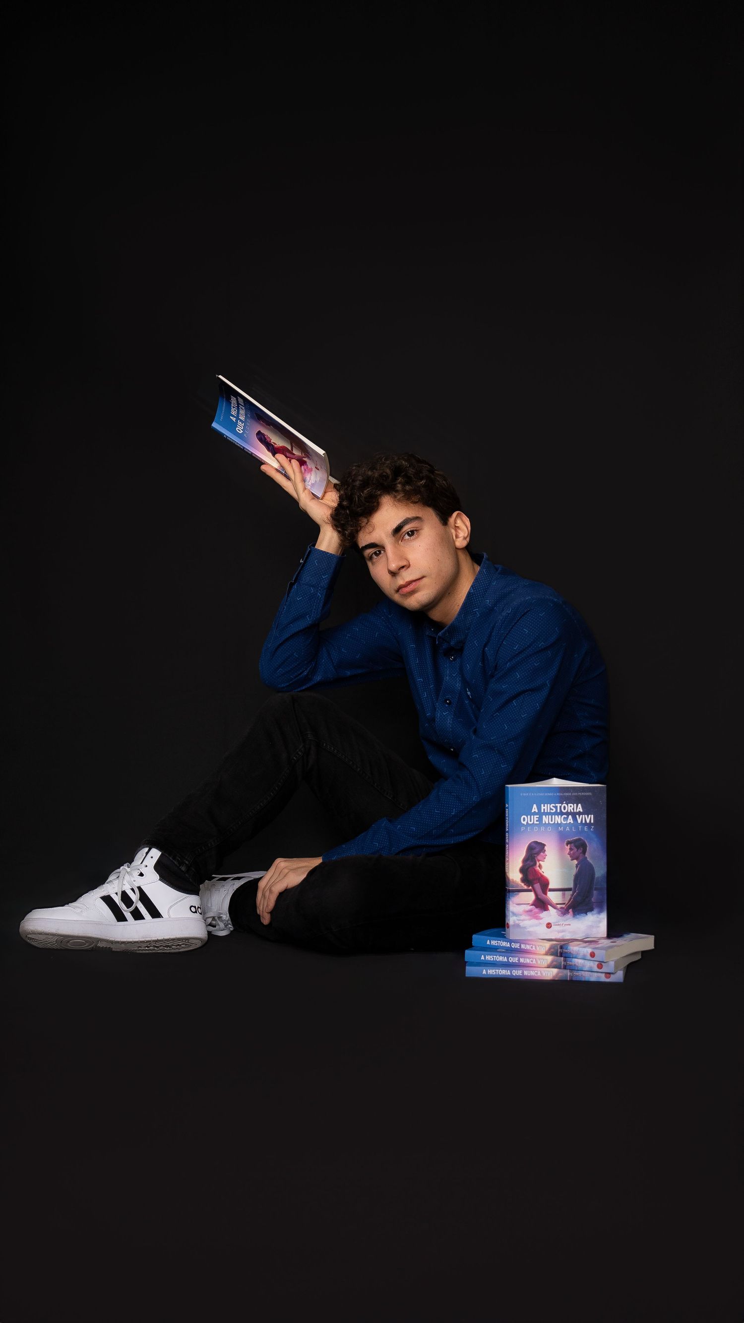 Person in blue shirt lying on floor with books against black background.