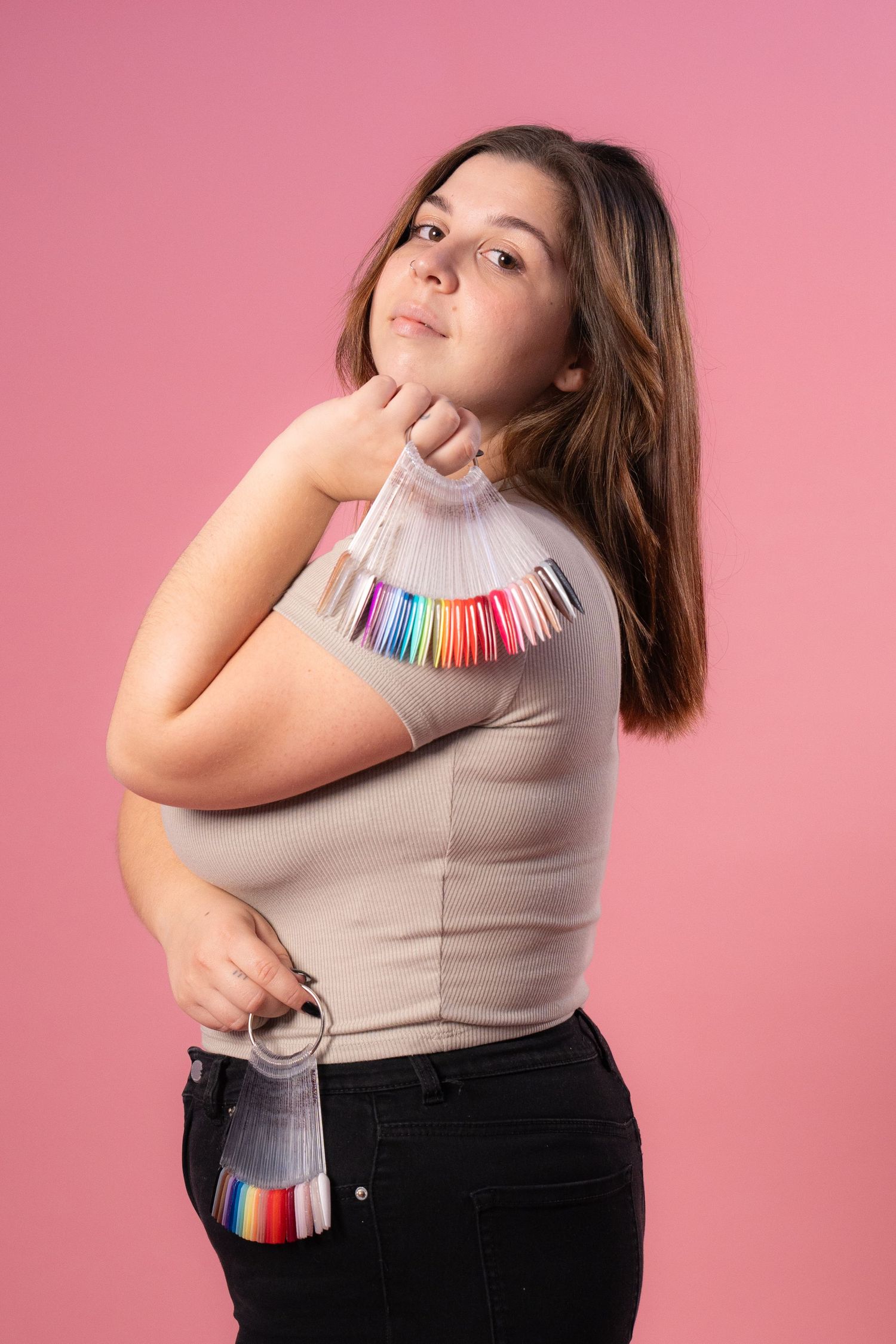 Model poses with colorful nail polish samples against pink background.