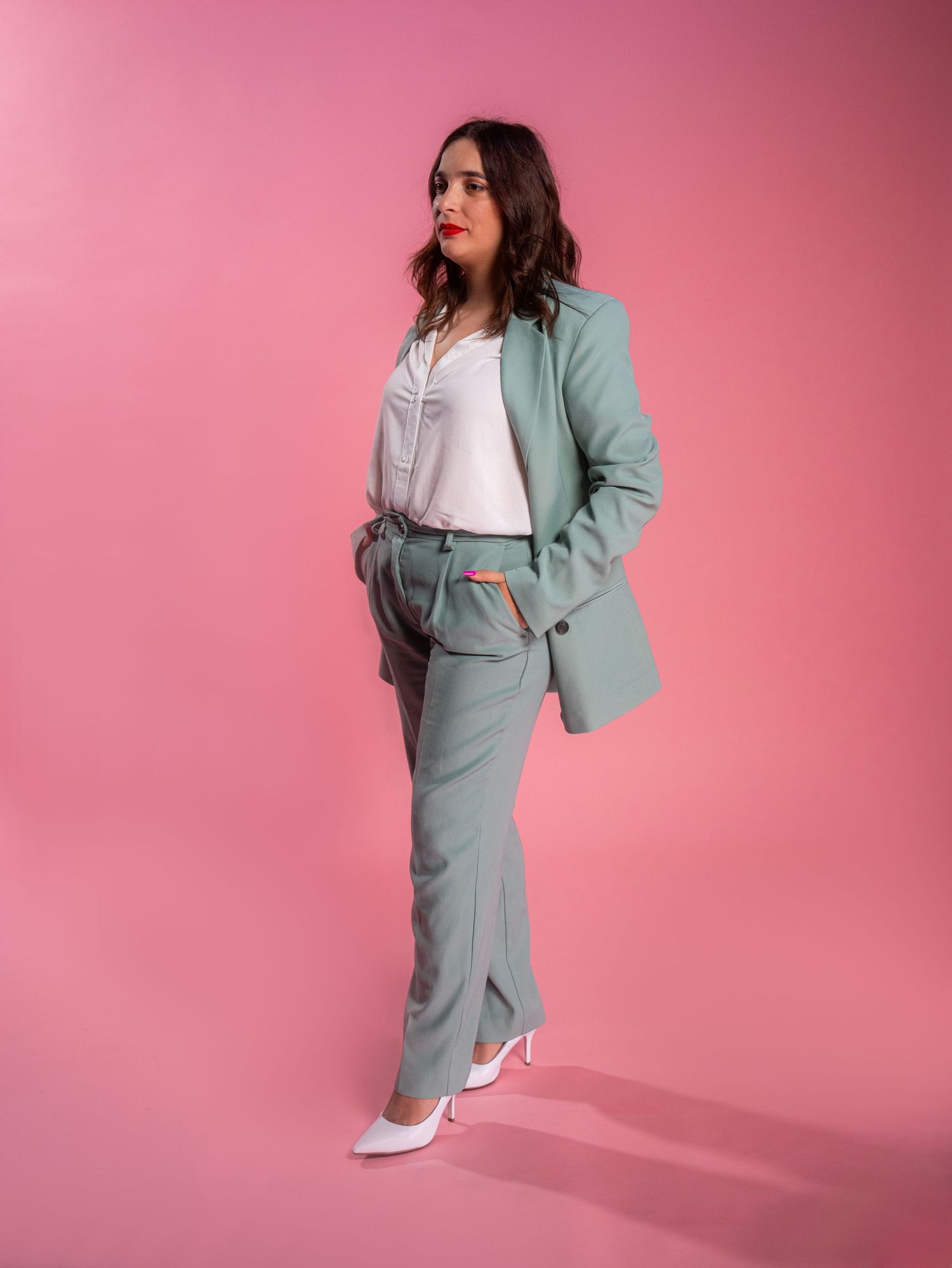 Stylish mint green business suit outfit photographed against pink studio background.