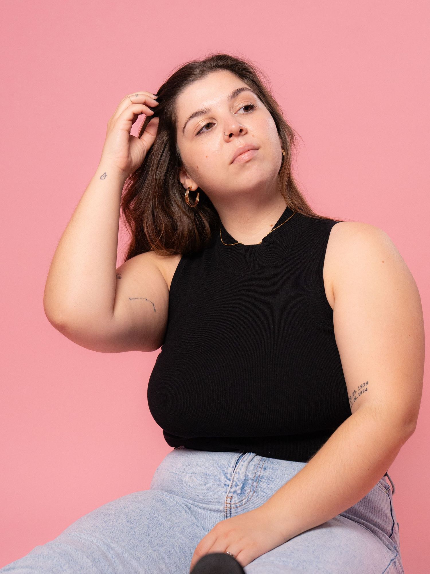 Model in black top poses confidently against pink studio background.
