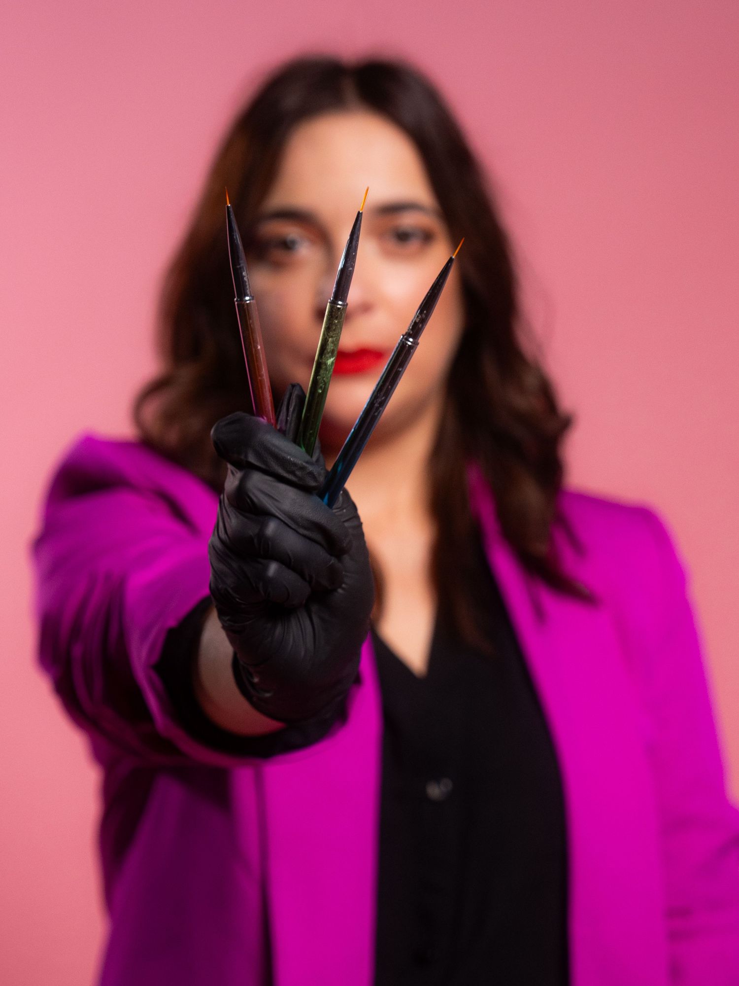 Person in purple blazer making hand gestures against pink background.