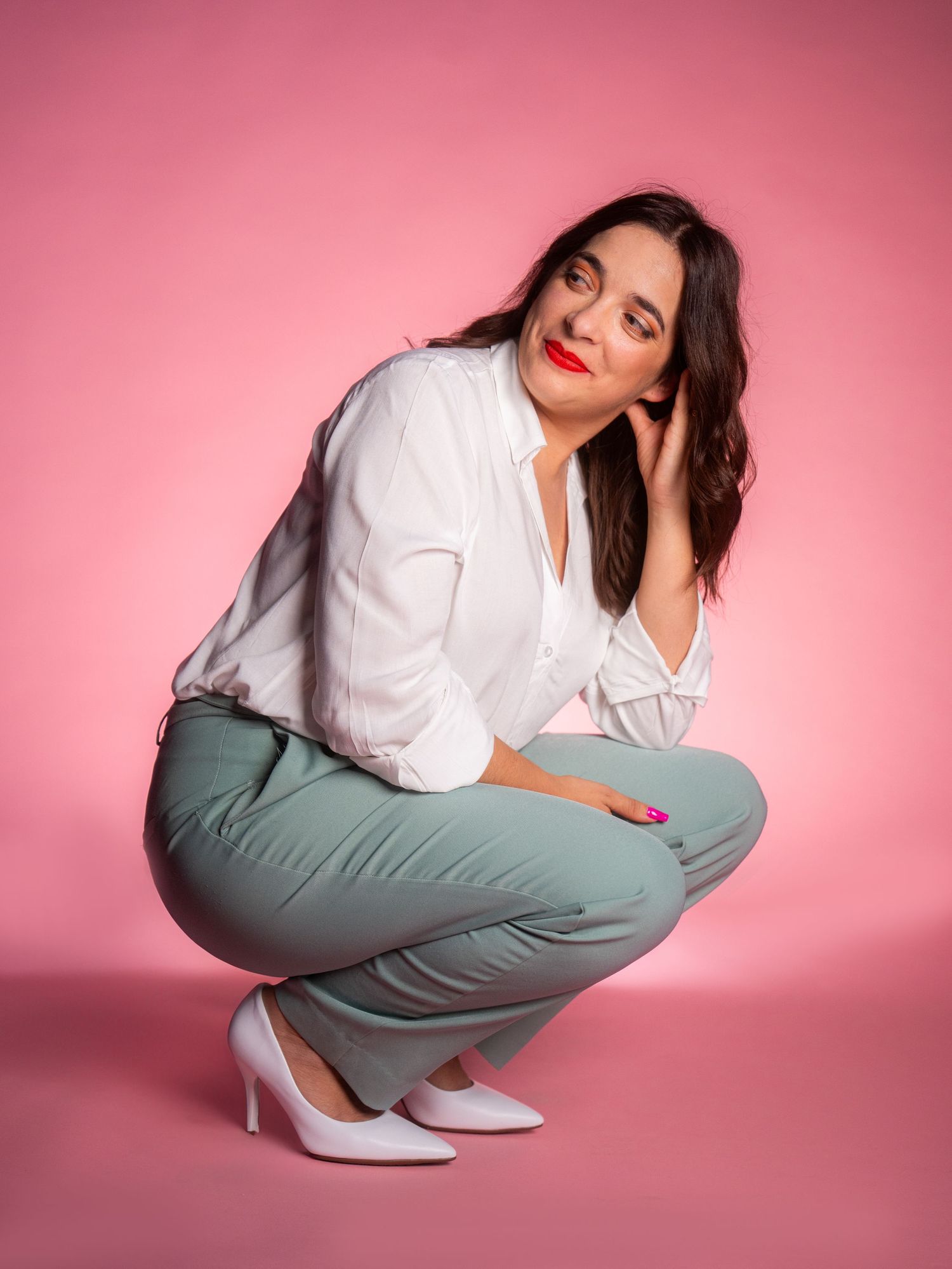 Professional poses in white shirt and sage pants against pink background.