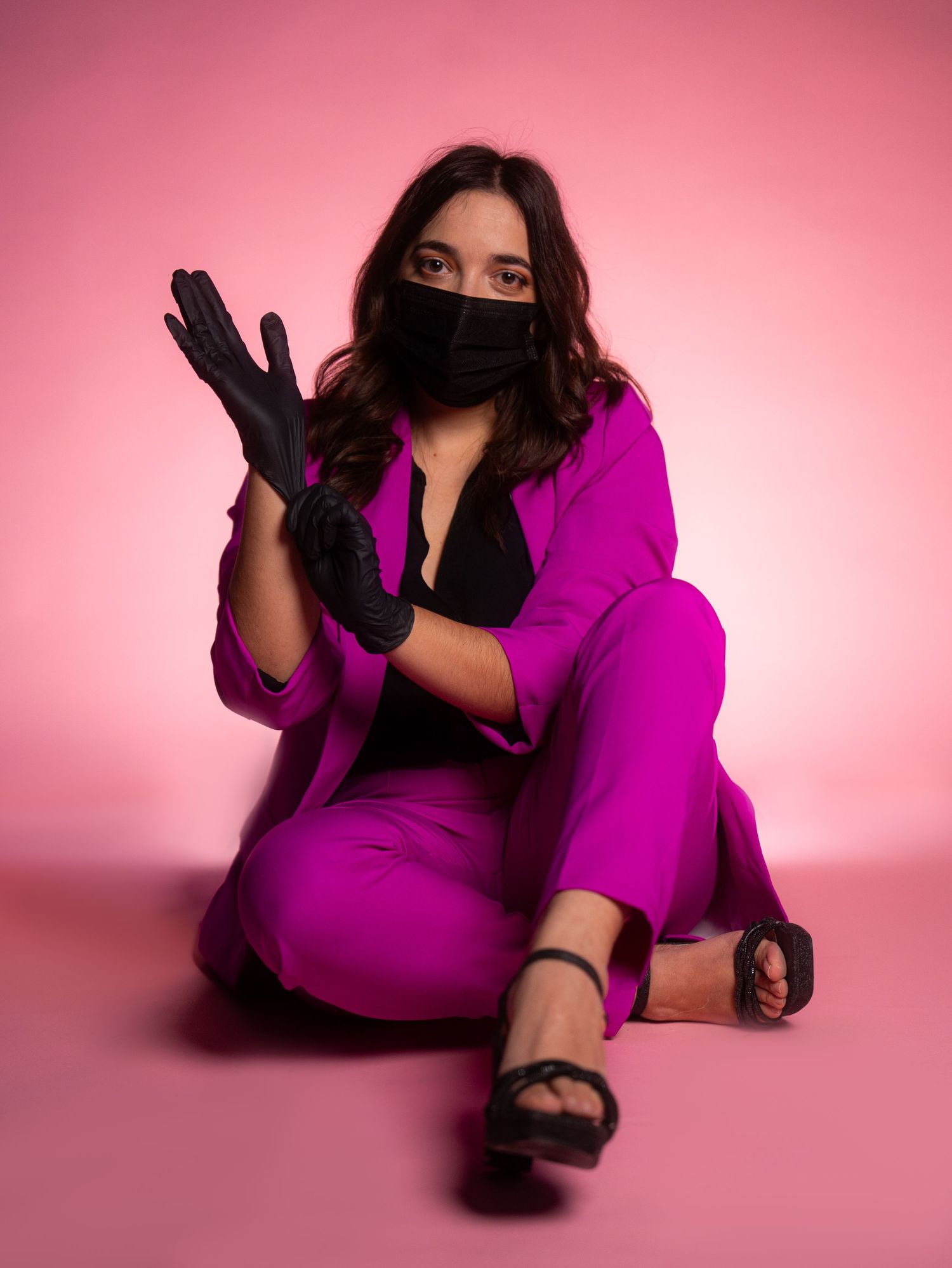 Creative poses on floor wearing purple outfit against pink studio backdrop.