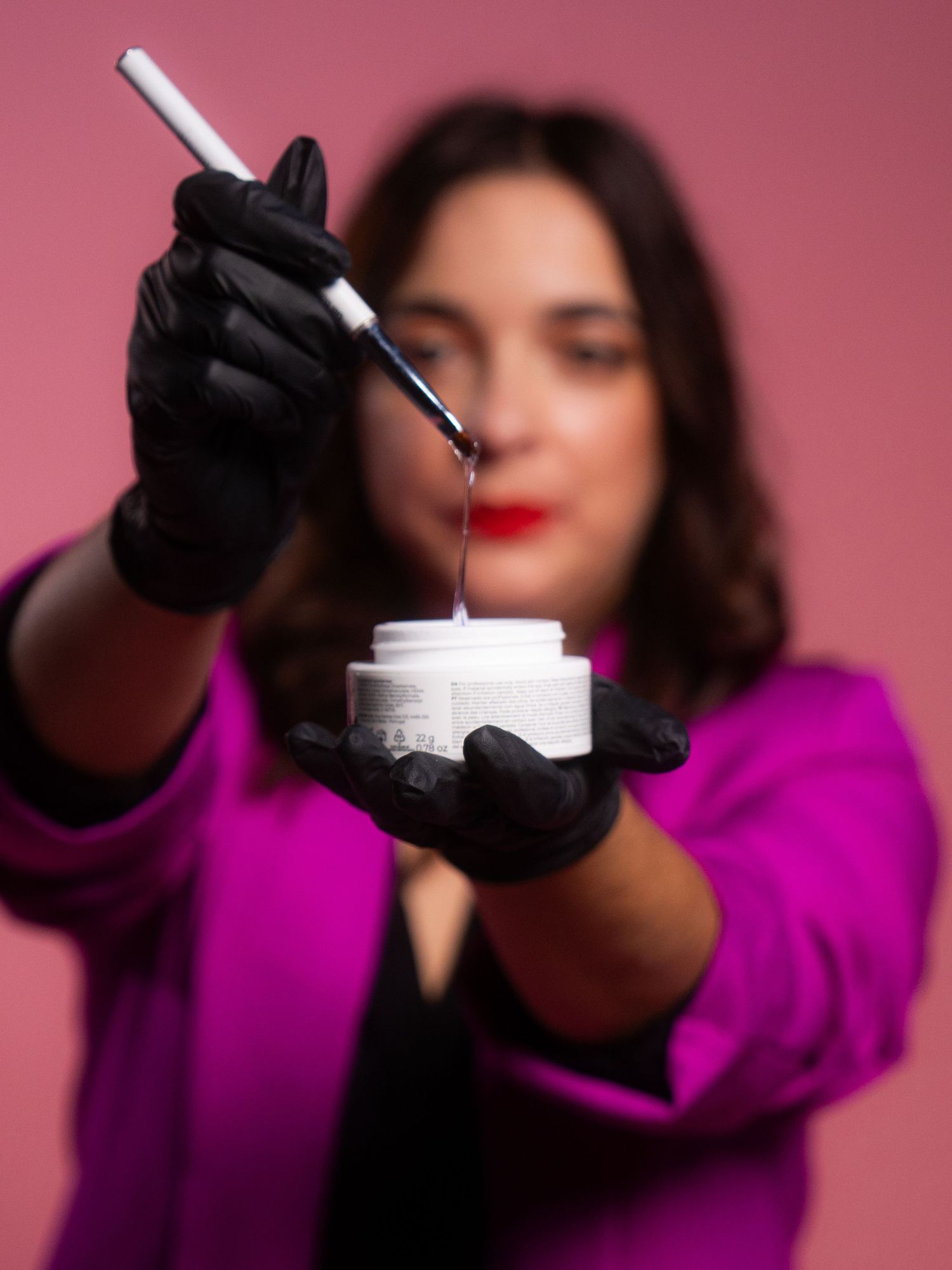 Hands in black gloves working with cosmetic products against pink background.
