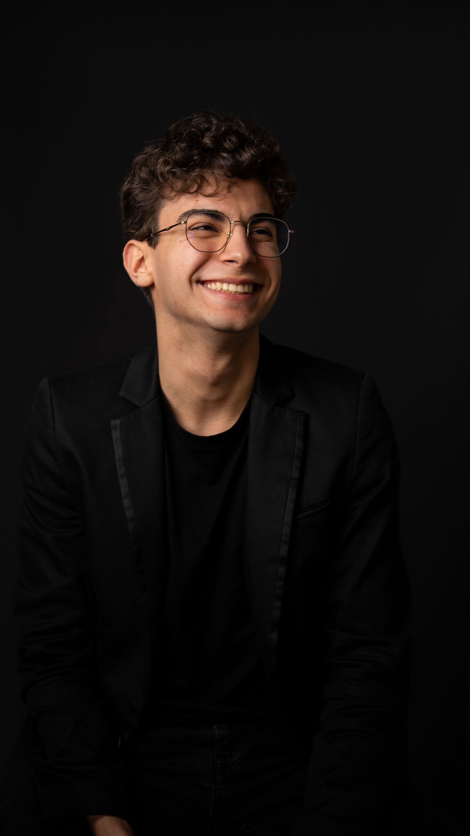 Portrait of person in black blazer smiling against dark background.