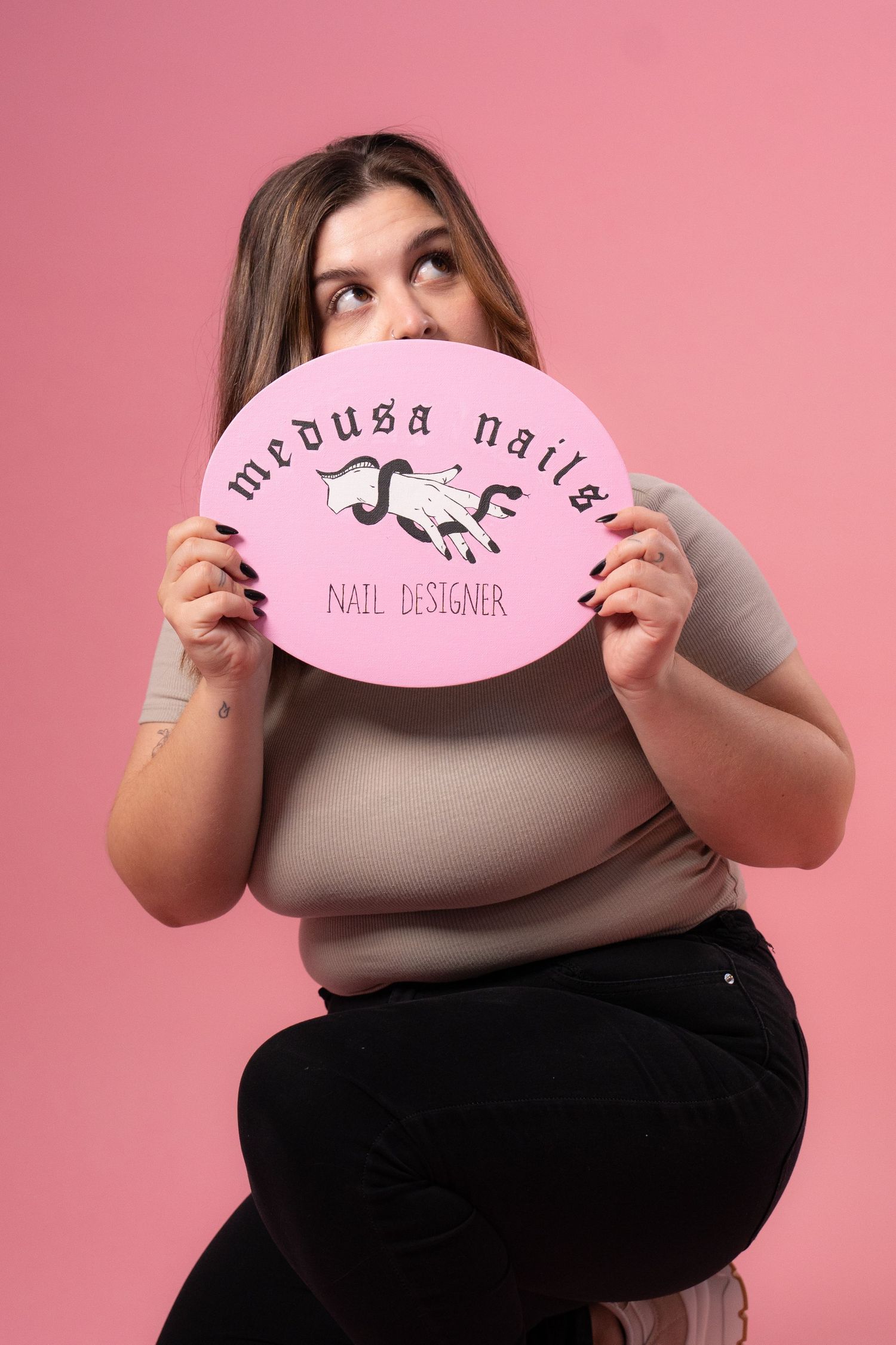 Model holding pink Medusa Nails branded sign against pink studio backdrop.