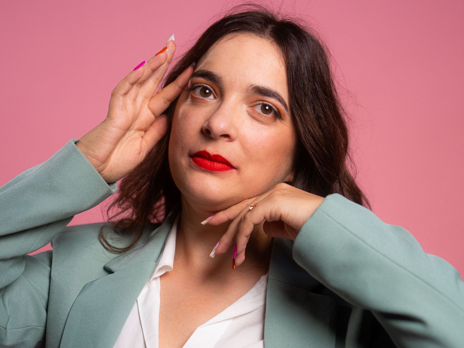 Dramatic poses in mint blazer against pink studio backdrop.