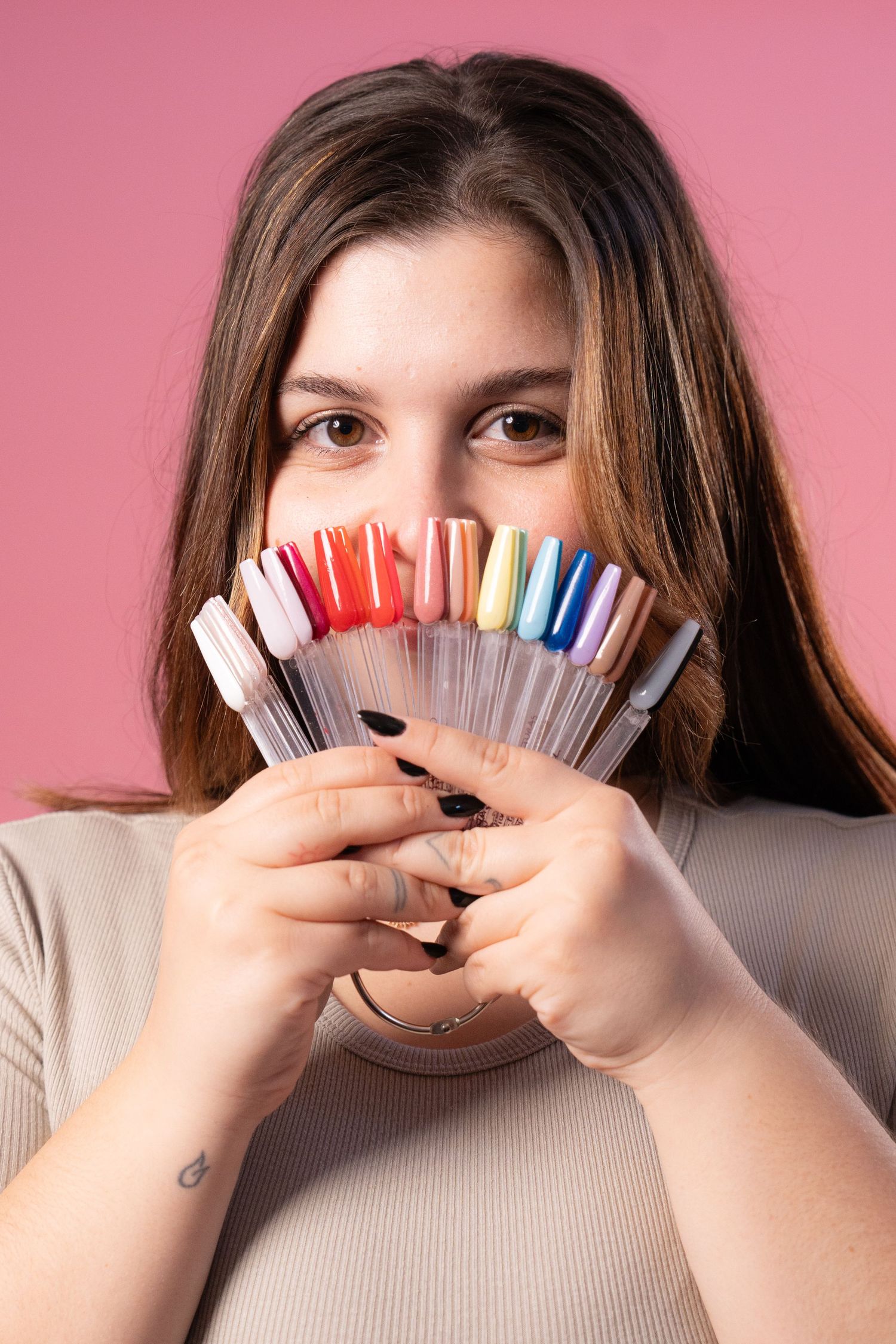 Model displays colorful nail polish samples in fan arrangement against pink backdrop.