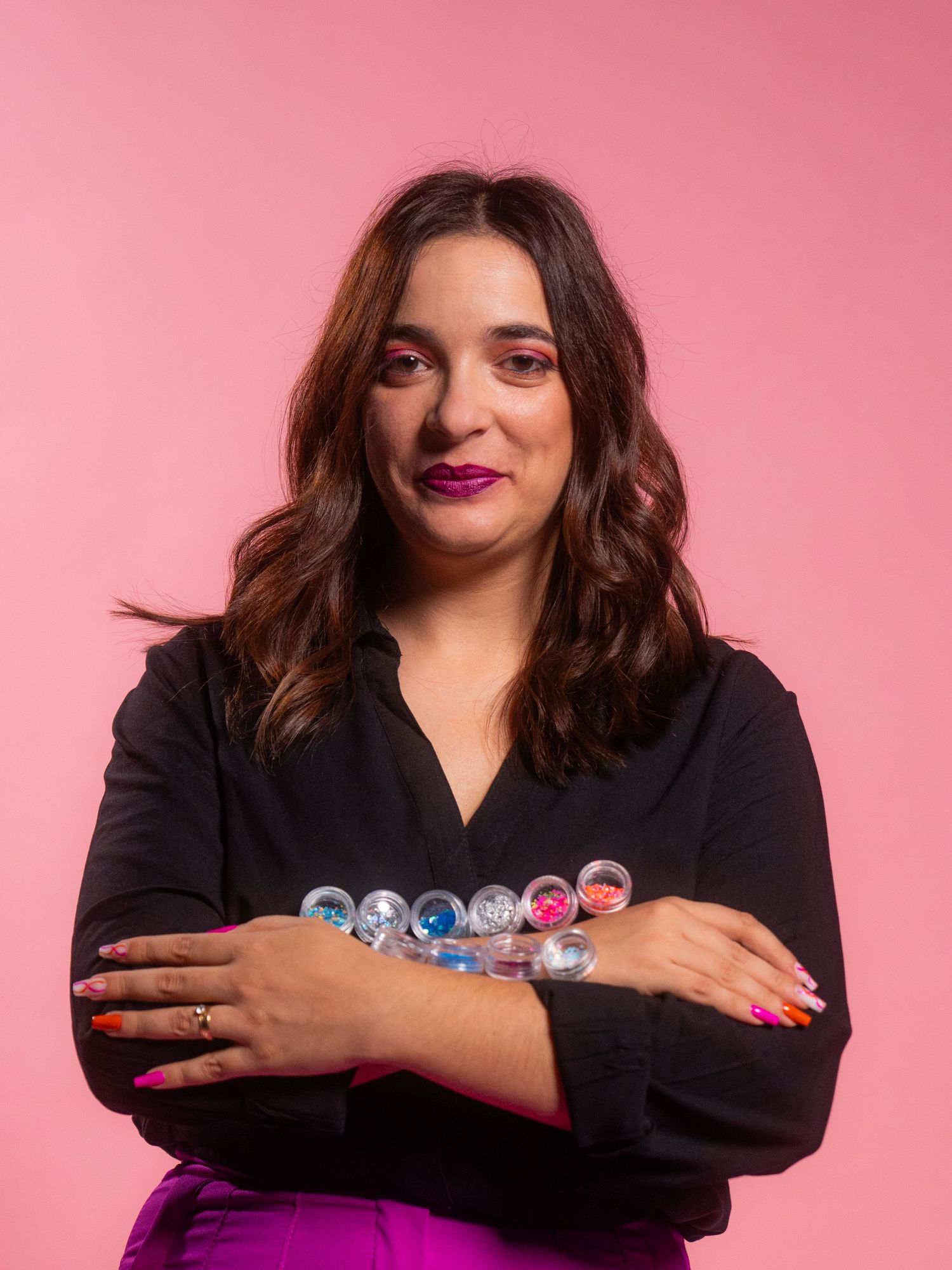 Professional photoshoot against pink backdrop showing person in black outfit holding small decorative items.