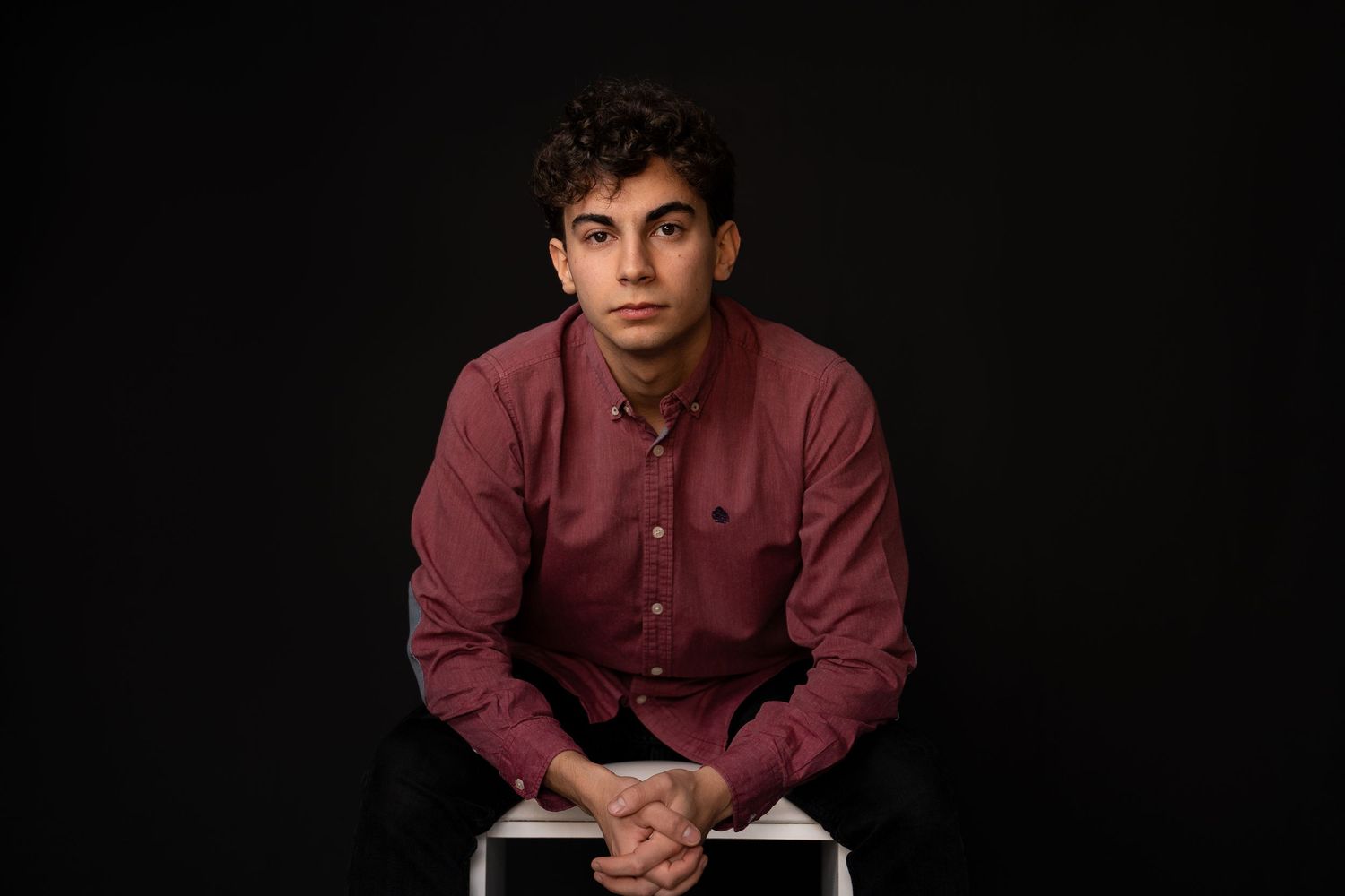 Studio portrait of person in burgundy shirt against dark background.
