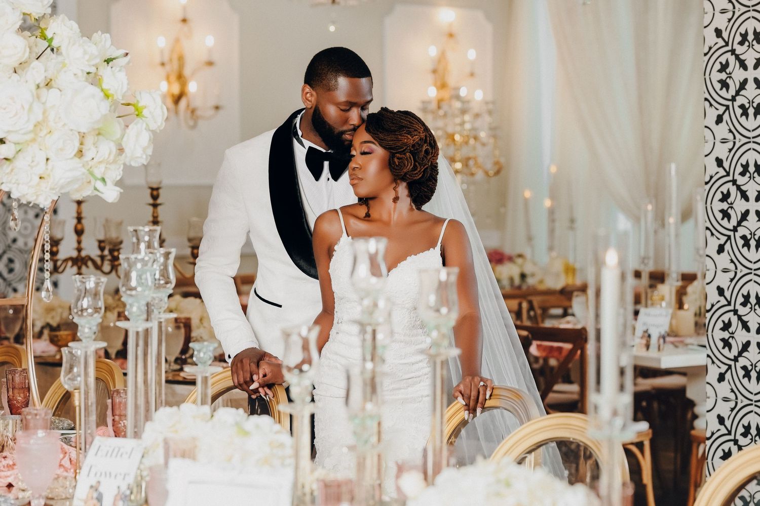 Romantic bride and groom share intimate moment at elegantly decorated wedding reception table with white flowers.