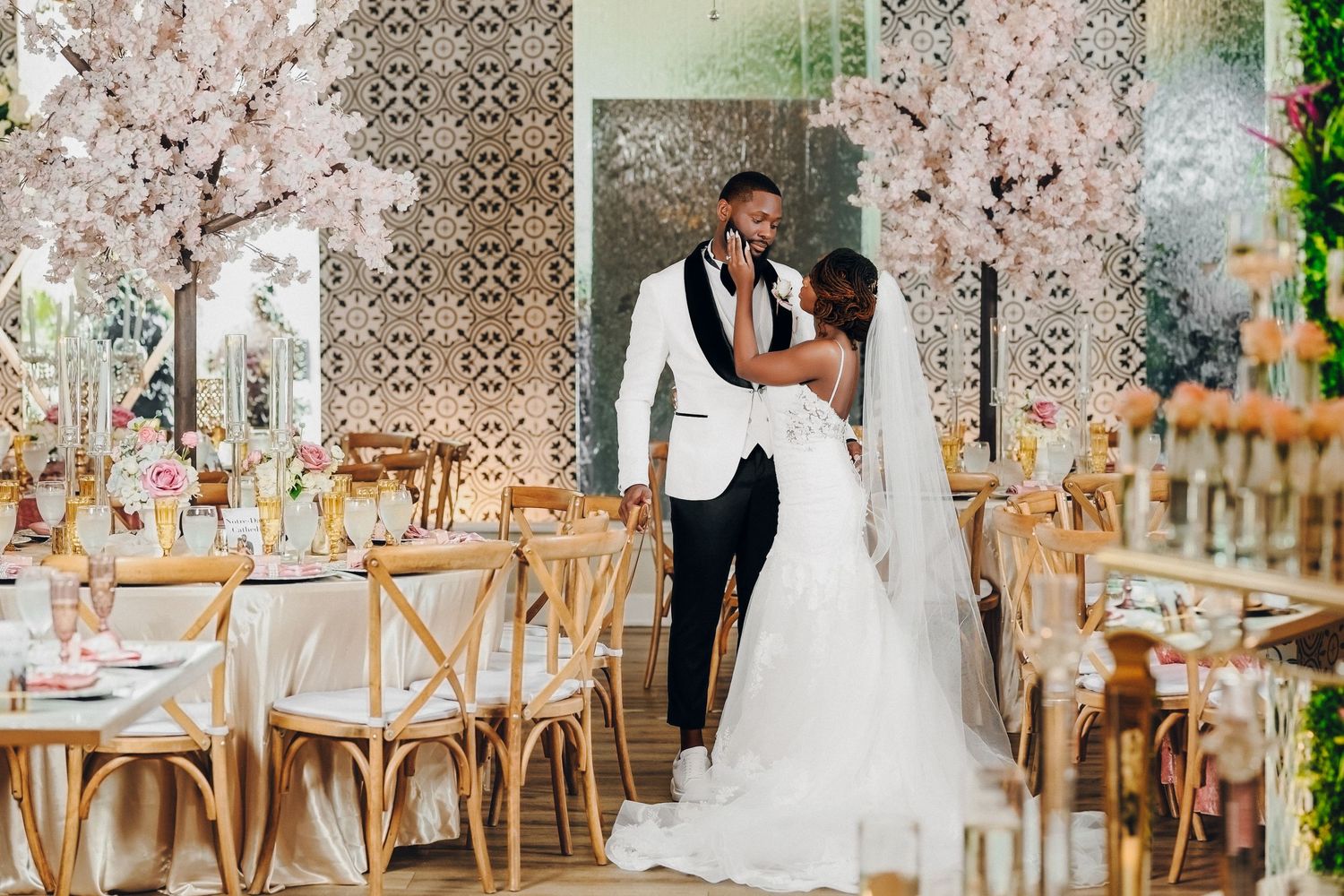 Bride and groom share romantic moment under cherry blossom trees in a sunlit elegant wedding venue.
