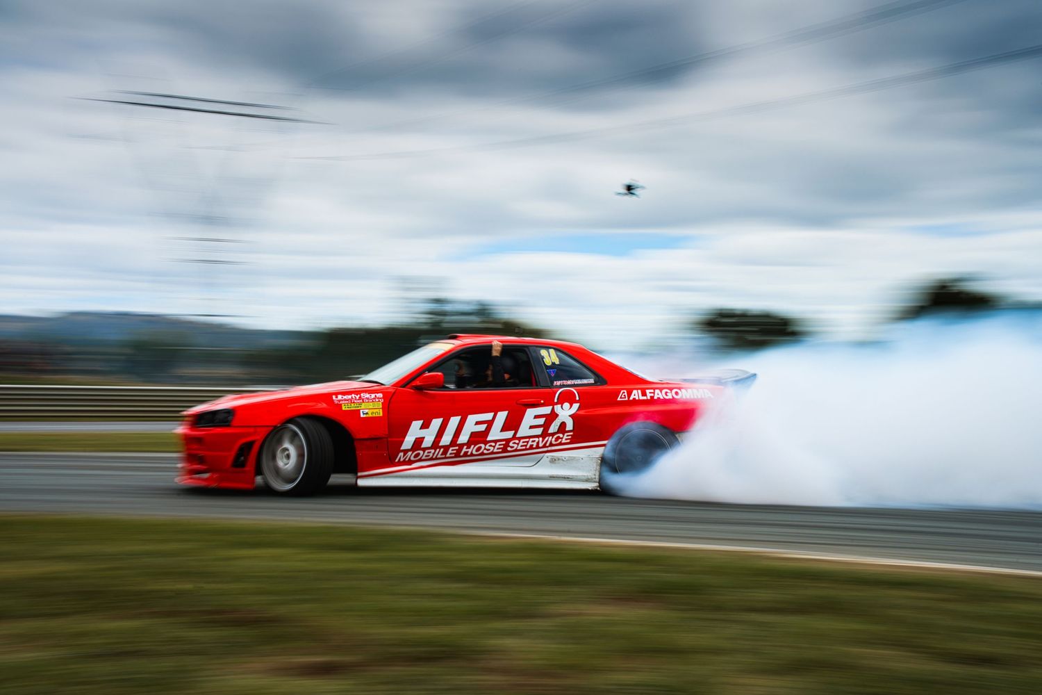 Red Hiflex race car creating dramatic tire smoke while drifting on track.