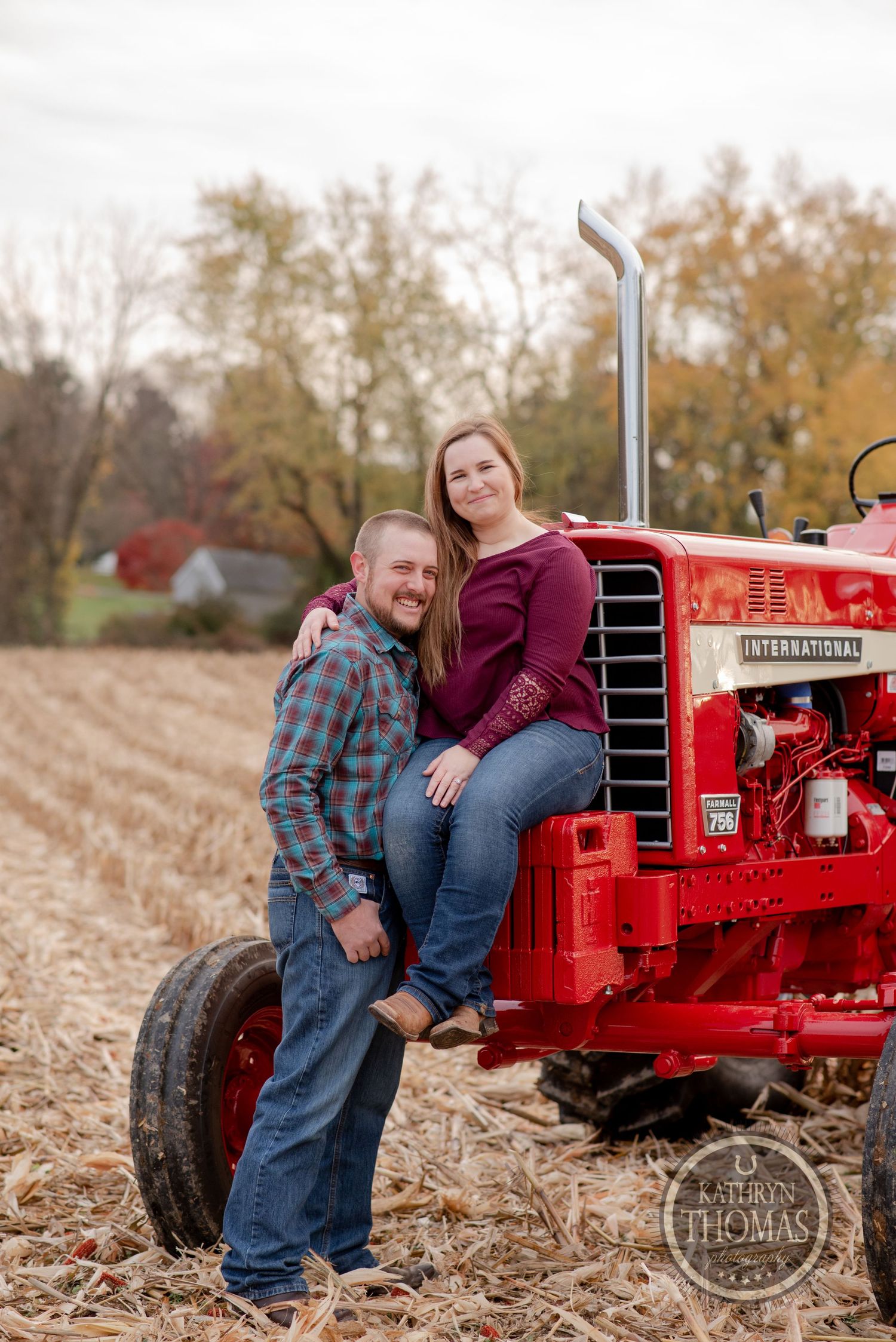 A couple poses together by a vintage red International tractor in a harvested field.