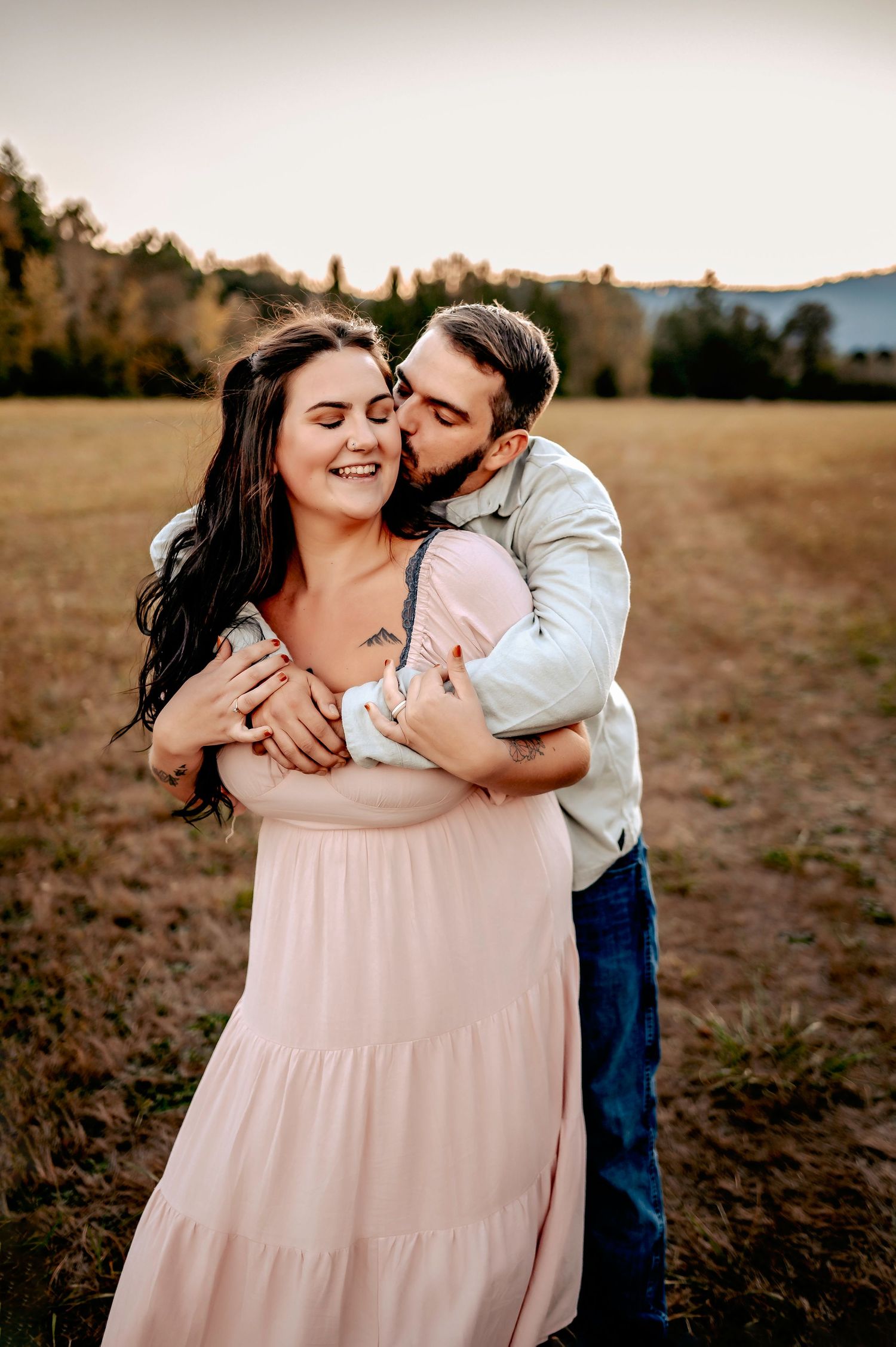 Intimate couple portrait in a field at sunset with soft pink dress and casual attire.