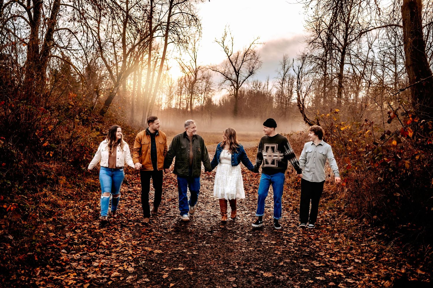Group of people walking in a line through autumn foliage at sunset.