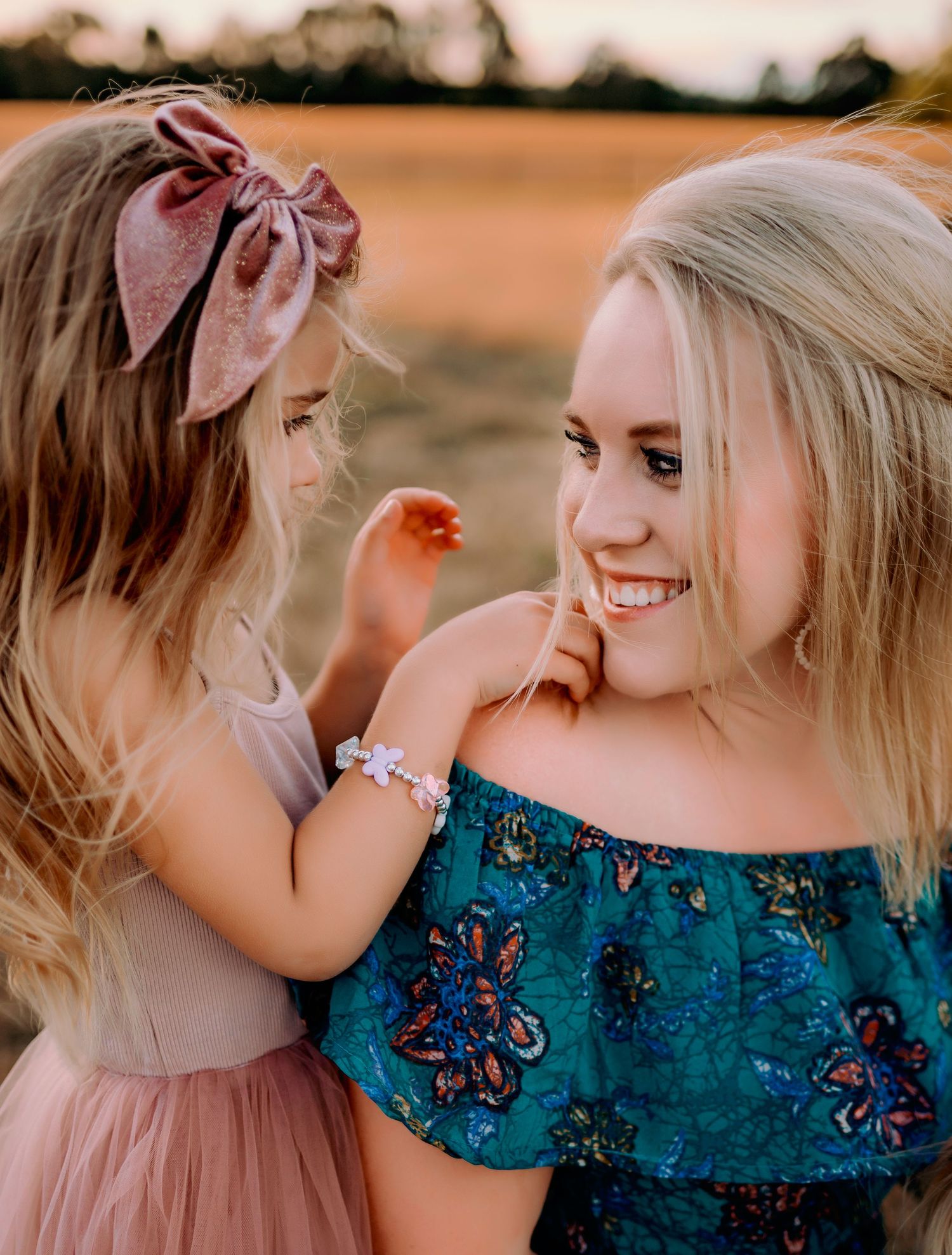 Sweet moment between child and woman in floral top during golden hour.