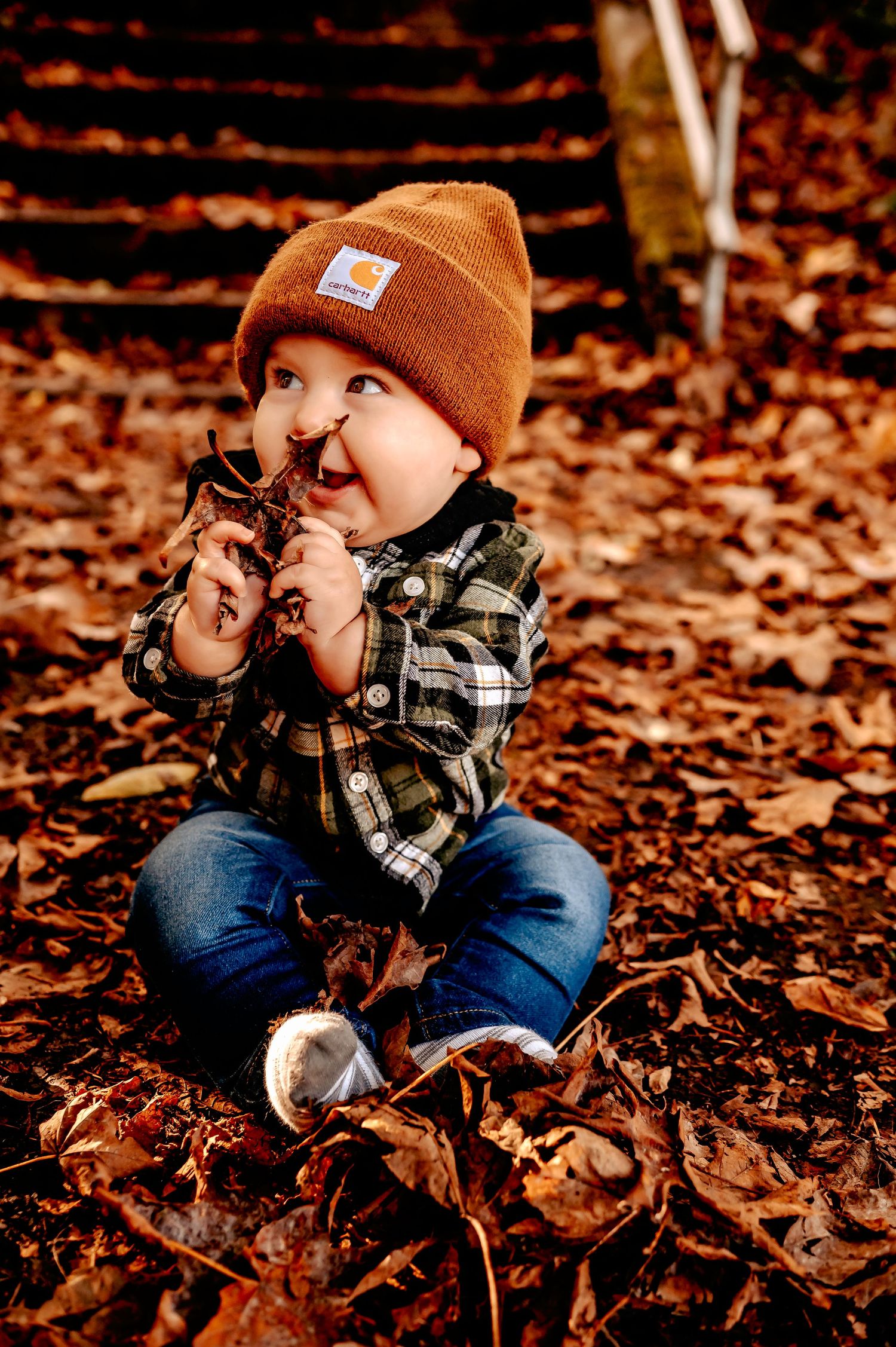 Small child in orange beanie plays in fallen autumn leaves.