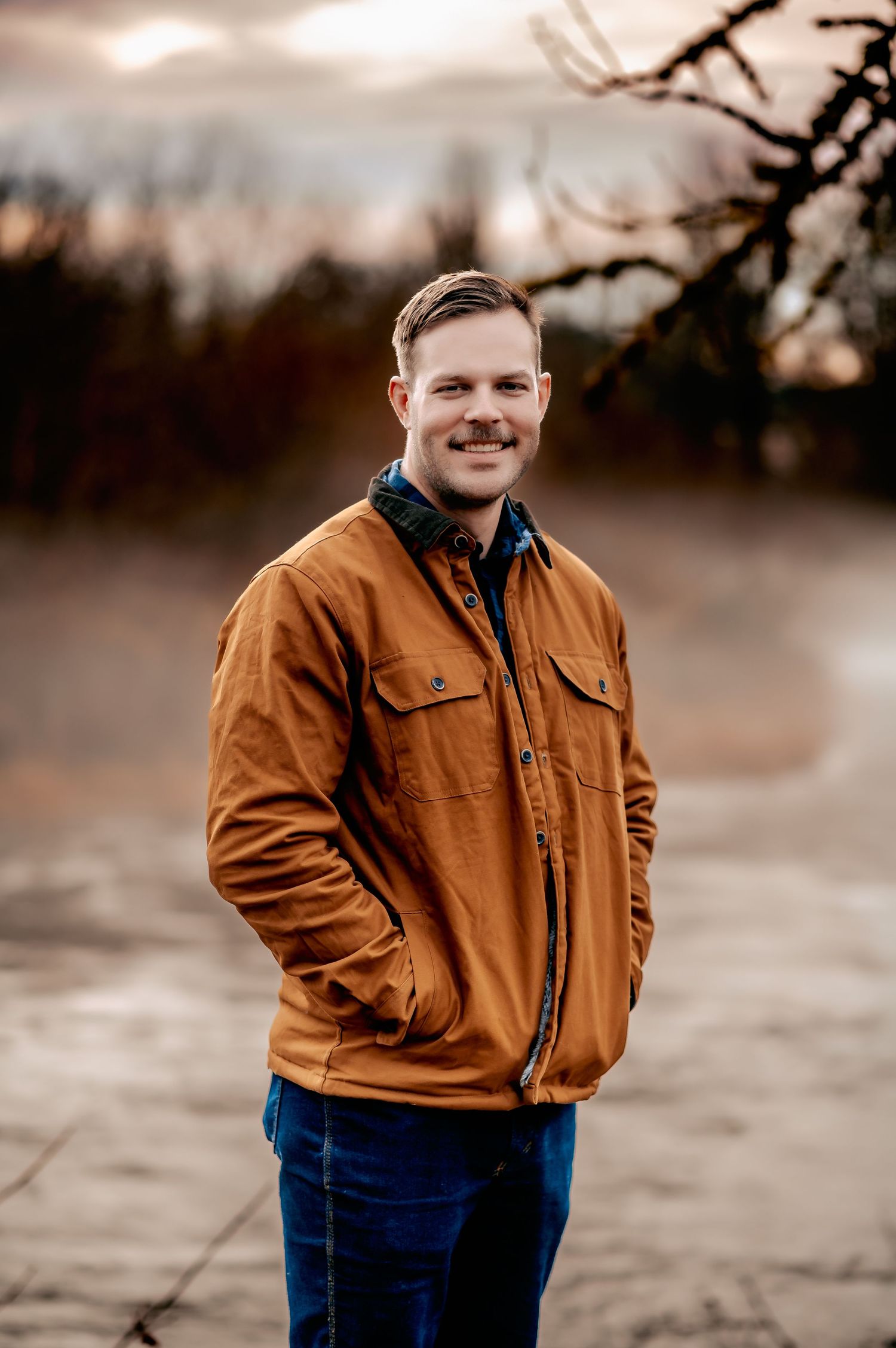 Person in brown jacket smiling outdoors during golden hour photography session.