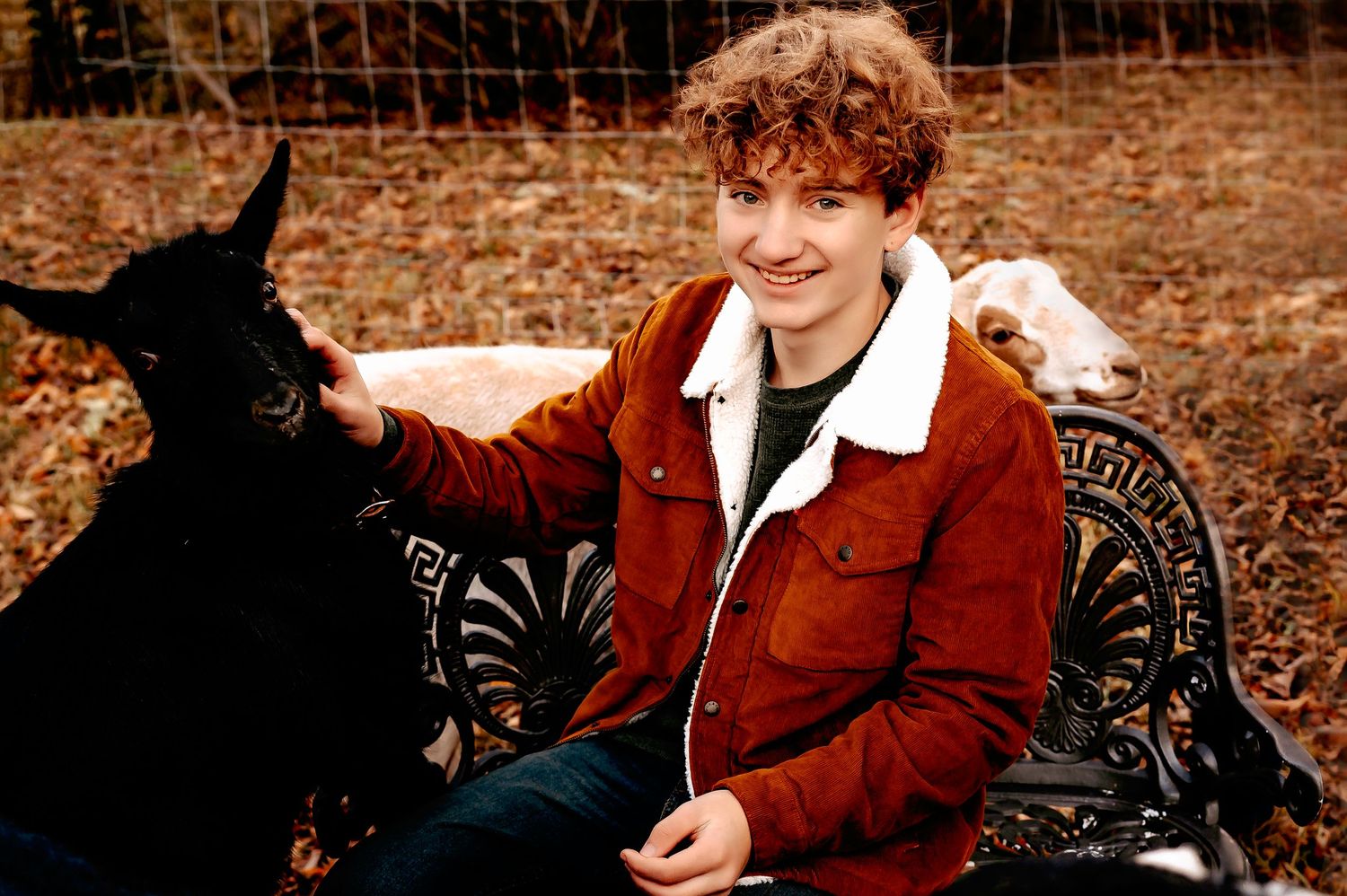 Person in red corduroy jacket sitting on ornate bench with black dog.