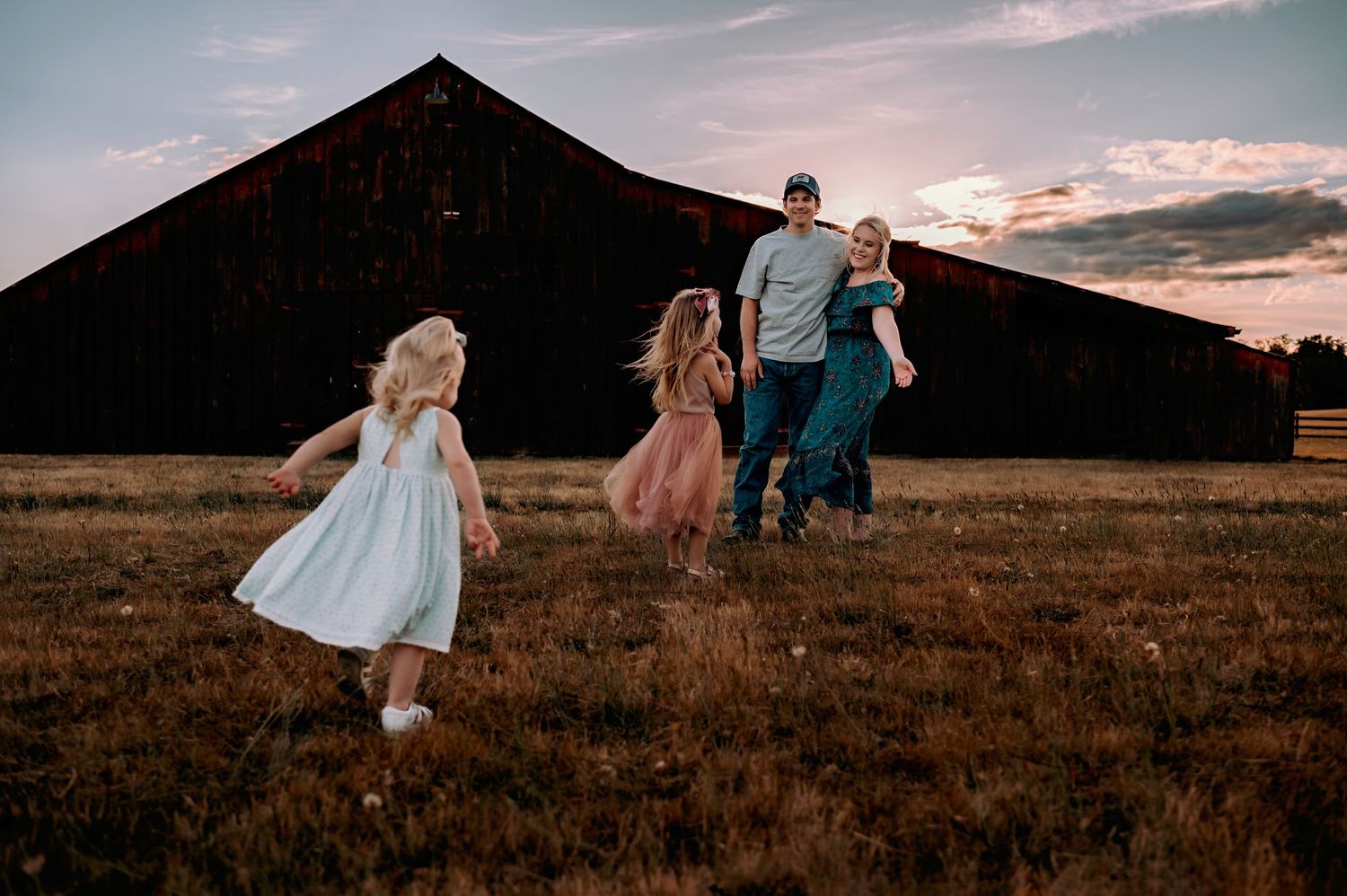 Family silhouetted against rustic barn during sunset.