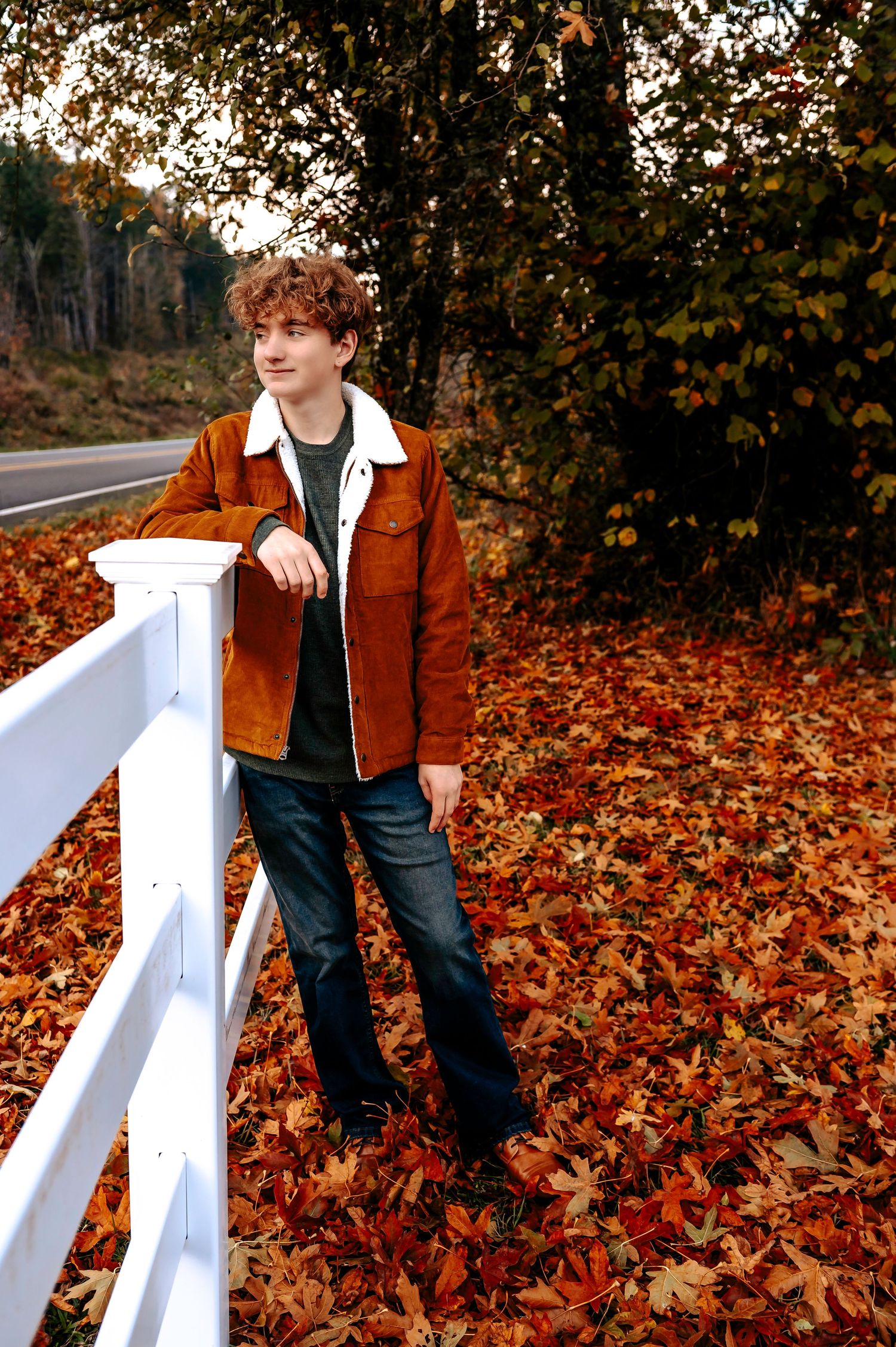 Autumn portrait against white fence with fallen leaves on ground.