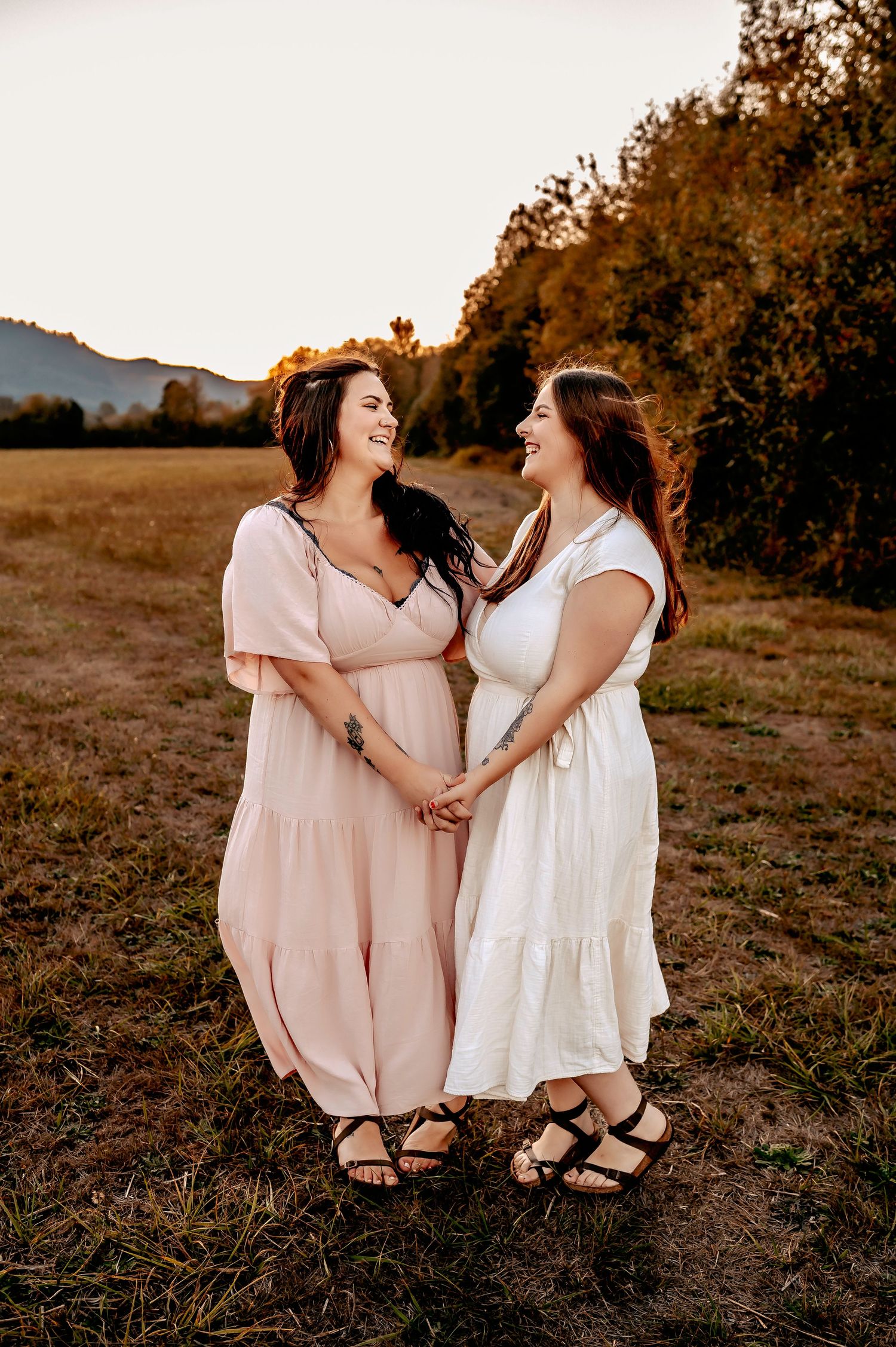 Two people in light pink and white dresses sitting together outdoors sharing a laugh.