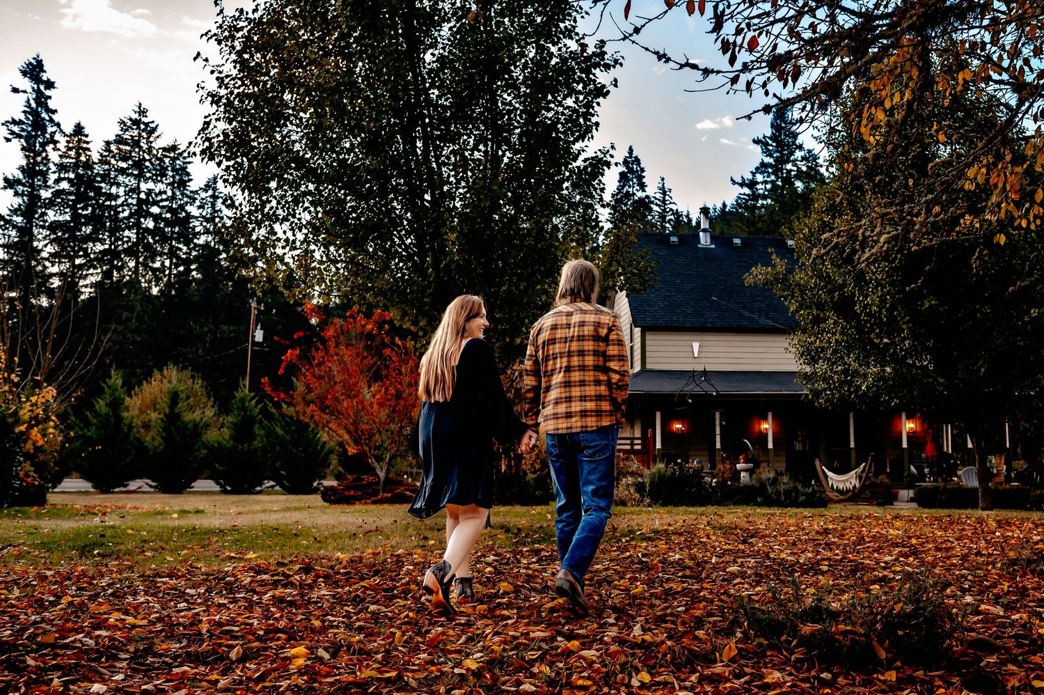 Couple walking through autumn leaves at rustic venue during sunset.