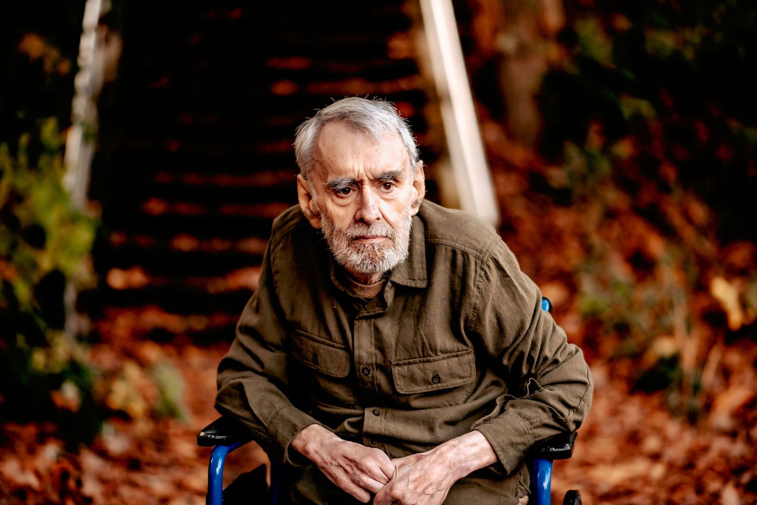 Senior man in olive jacket poses thoughtfully outdoors during autumn.
