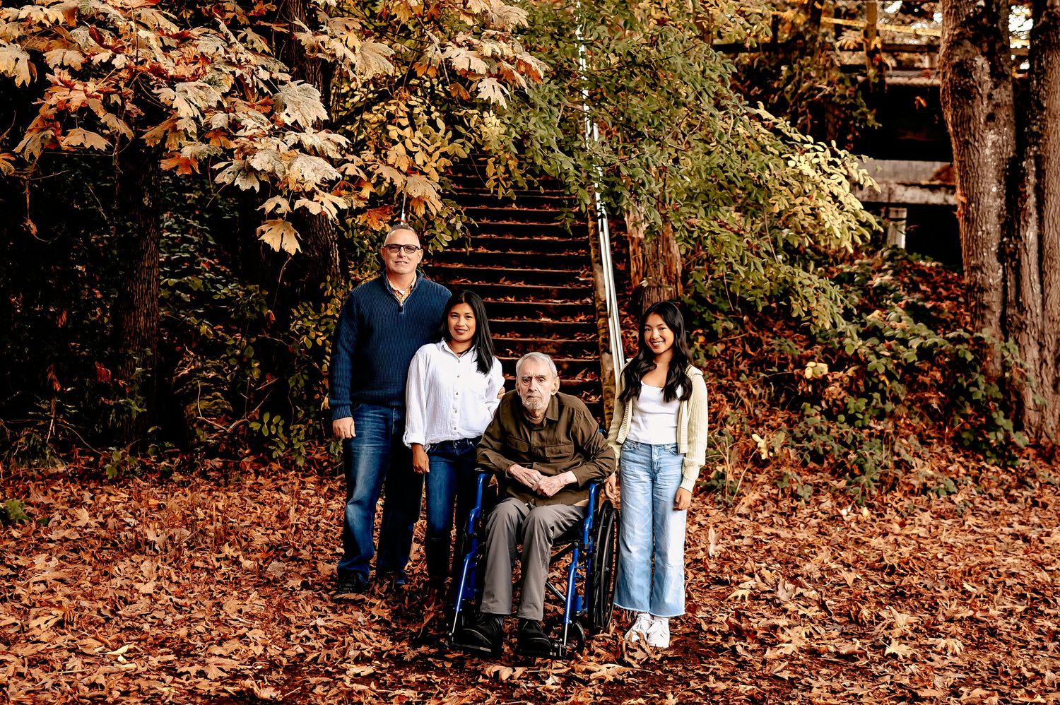 Group poses for casual portraits on leaf-covered hillside in fall setting.