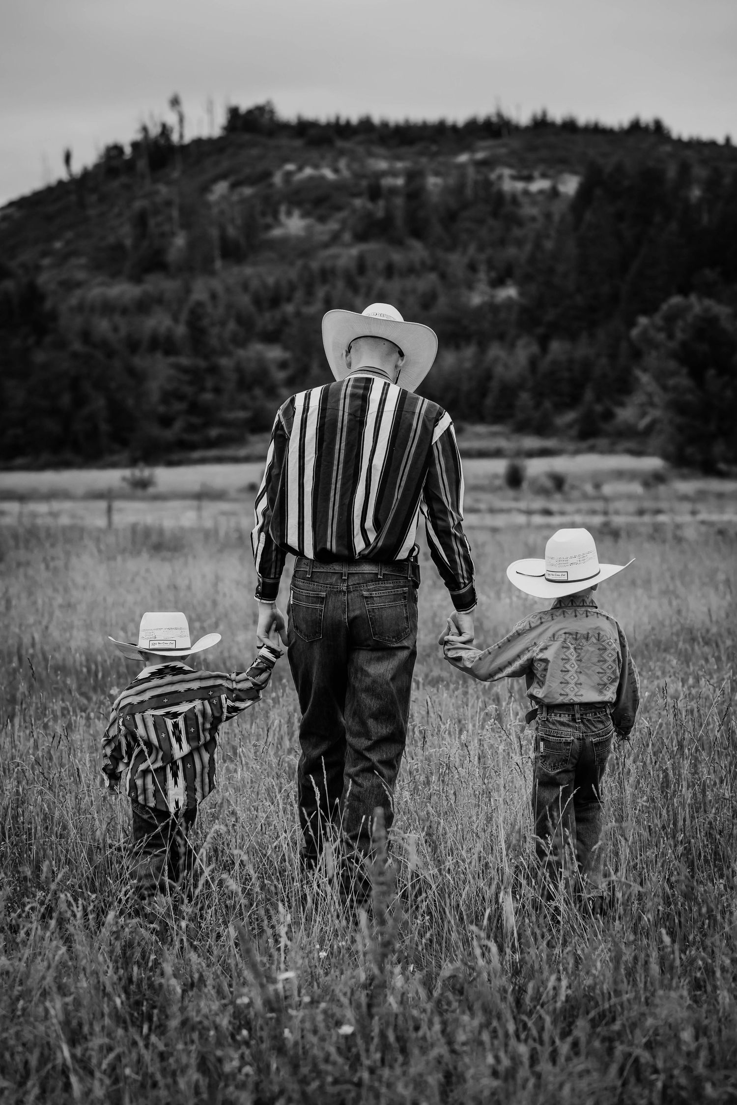 A group wearing cowboy hats walks through a tall grass field in black and white.