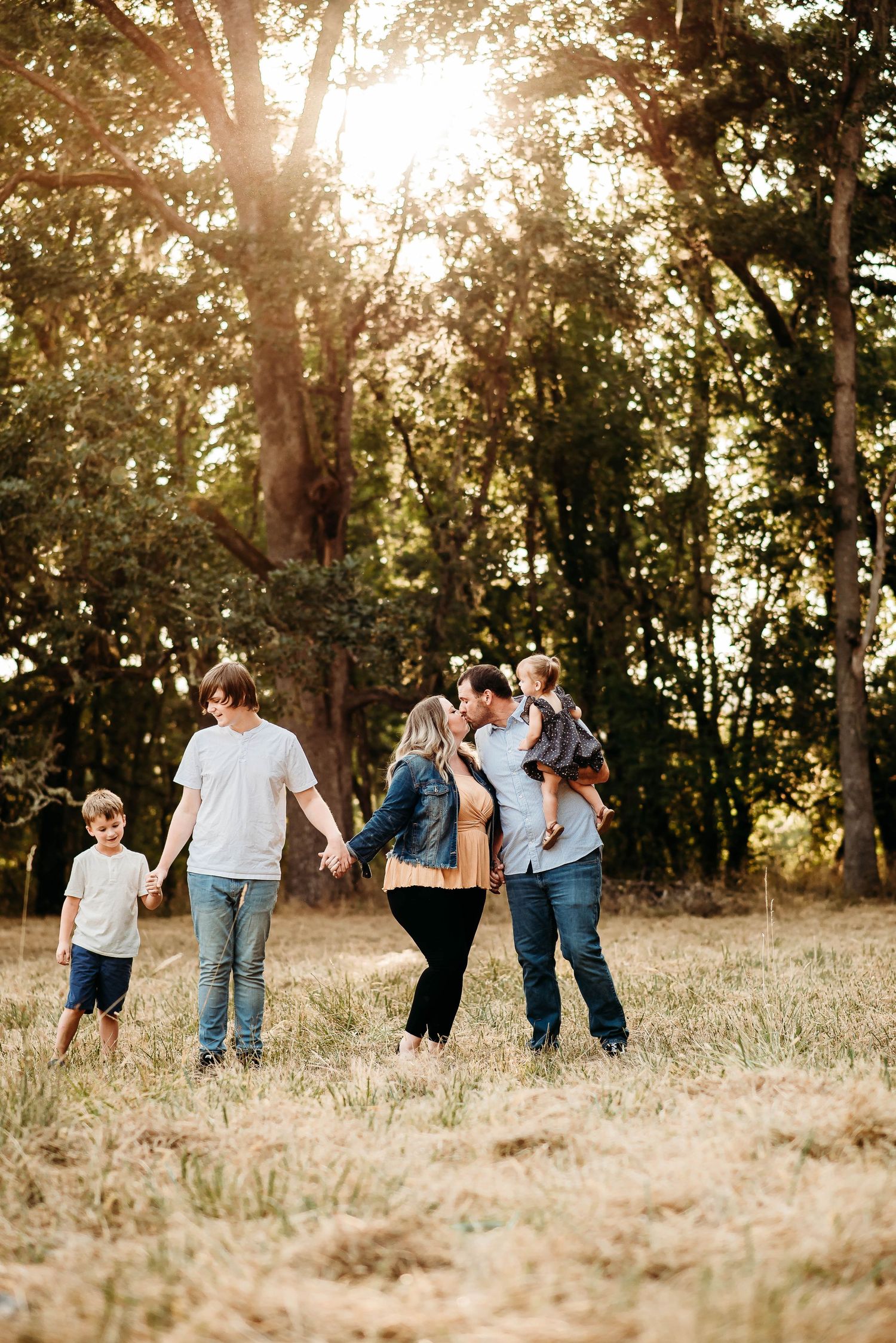 Family walking together at sunset in a golden field with trees.