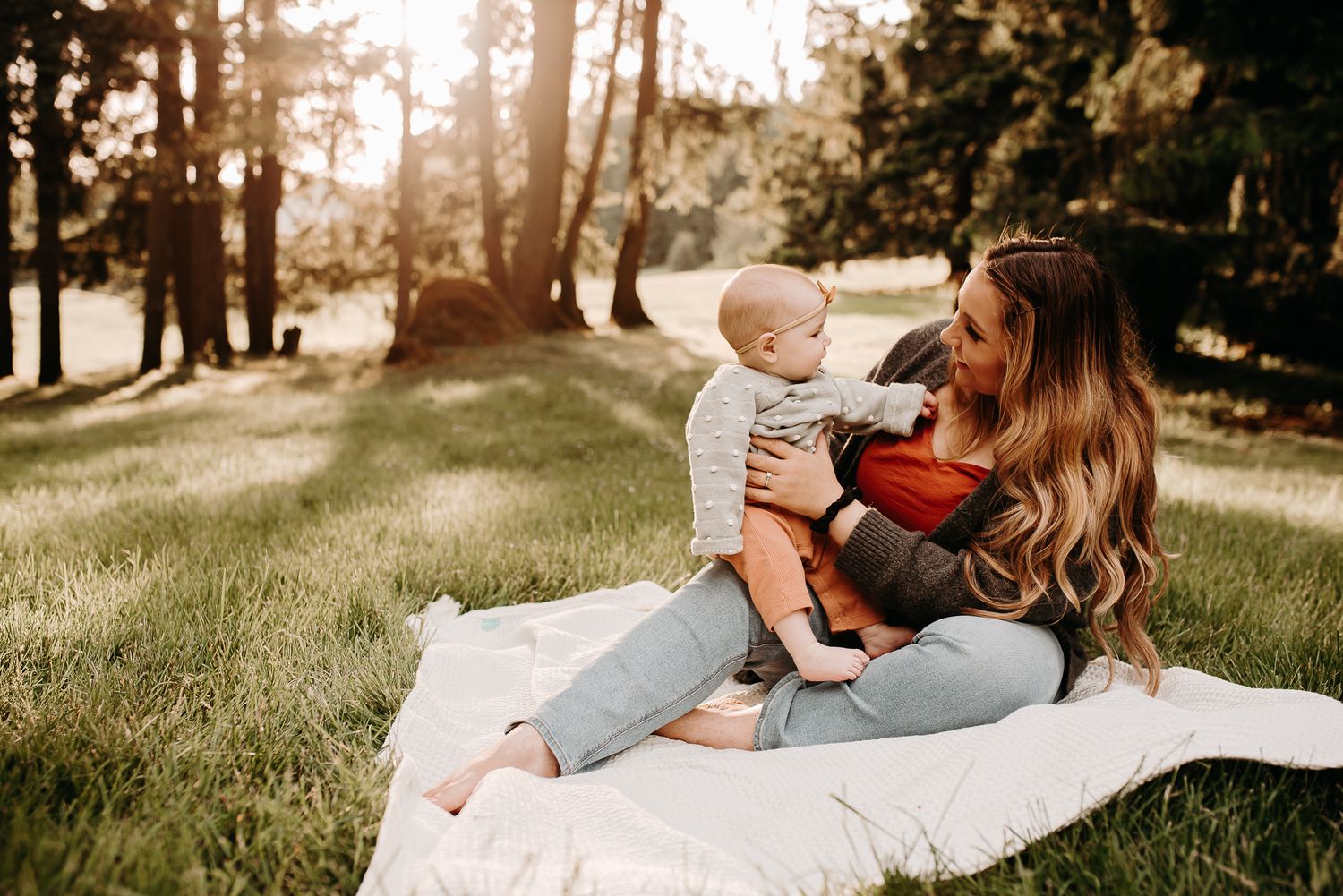Family lying on a blanket in a sunlit forest setting during golden hour.