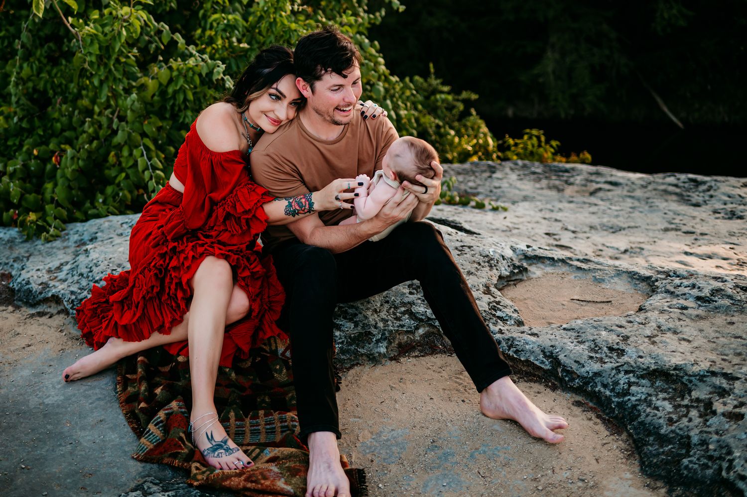 Casual family portraits on rocky ground with vibrant red dress creating visual contrast.