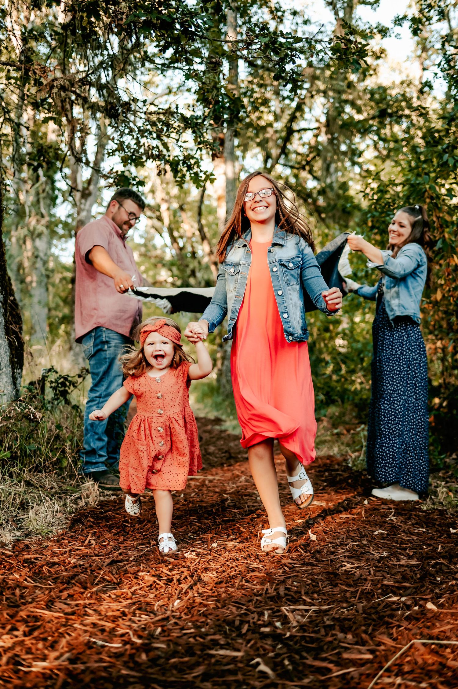Family in coordinating coral and blue outfits plays joyfully among trees in autumn setting.