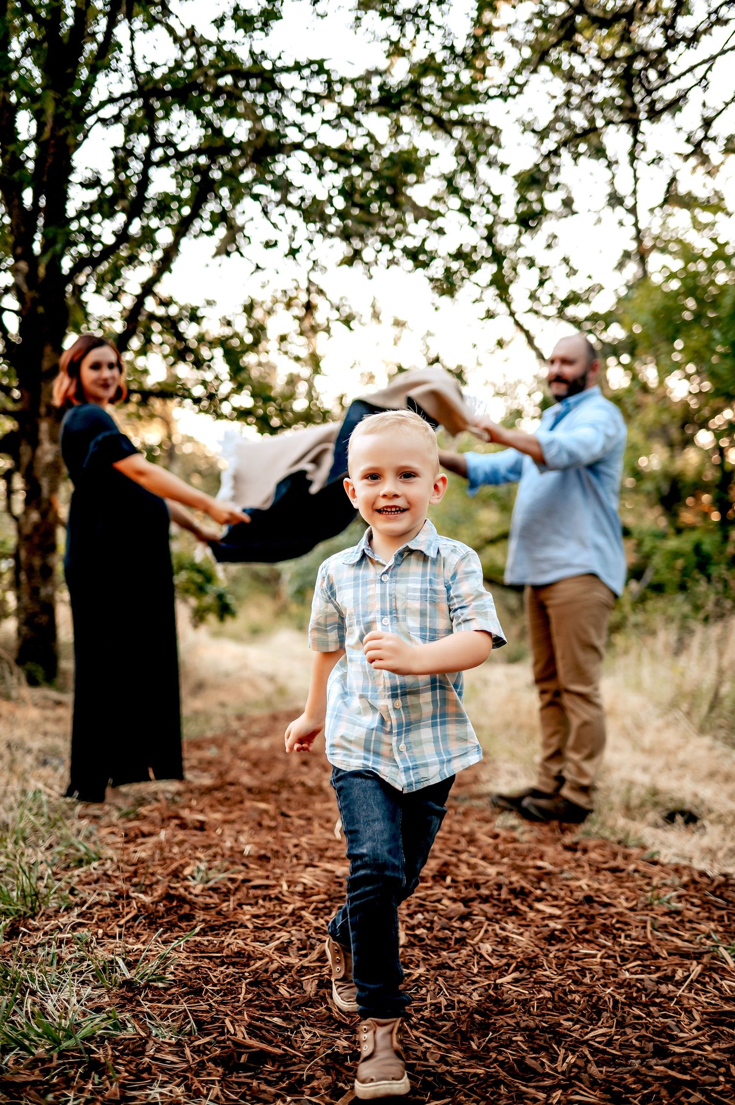 A playful family photo session in a wooded area with mulch ground cover during golden hour.