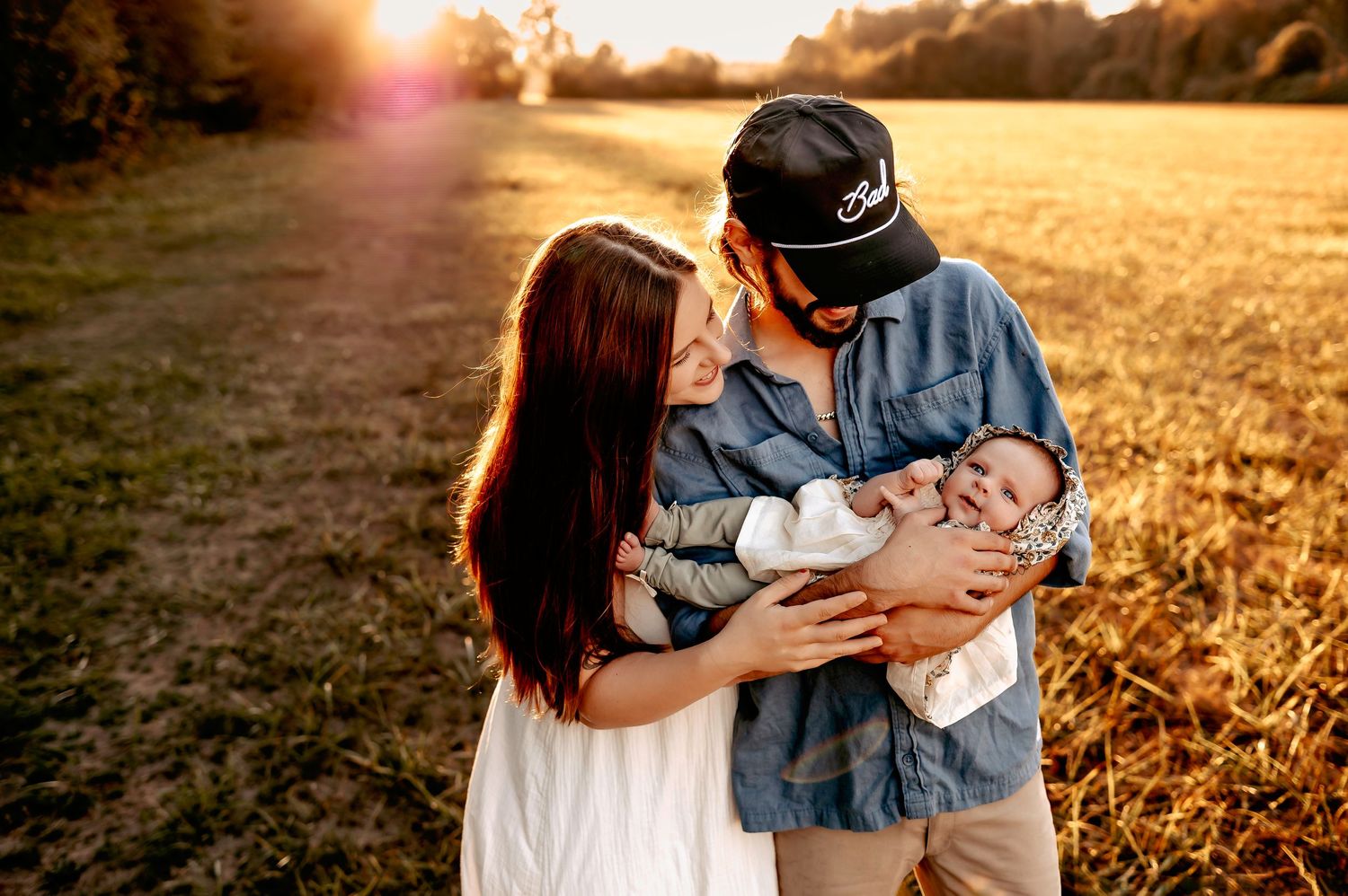 Loving family moment captured during sunset photoshoot in golden field.