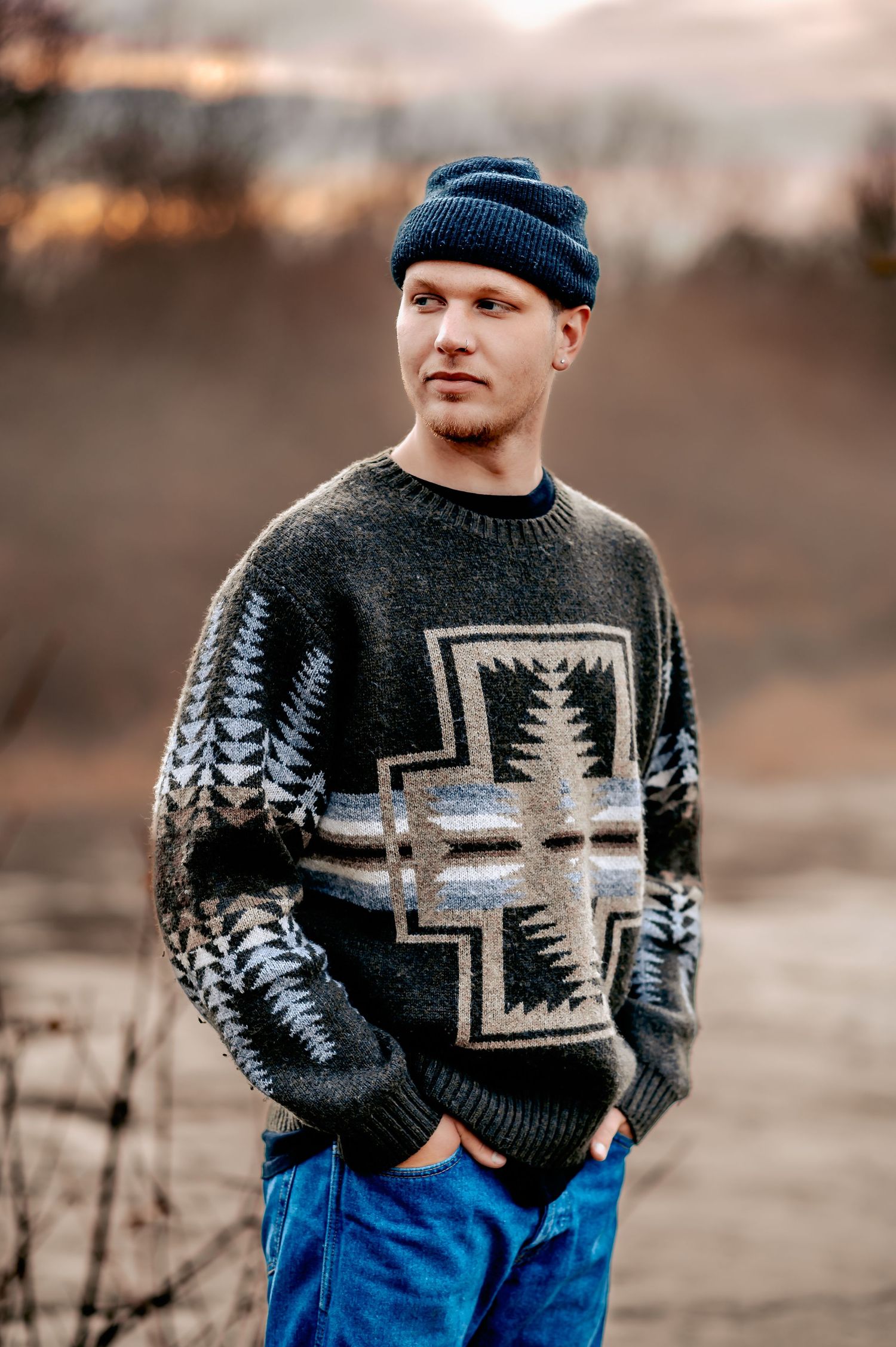 Person wearing a dark patterned sweater with geometric designs and a beanie hat in an autumn setting.