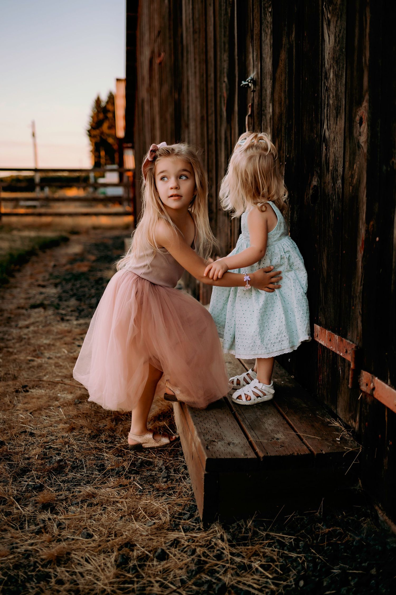 Two young children in tulle dresses playing on wooden porch at sunset.