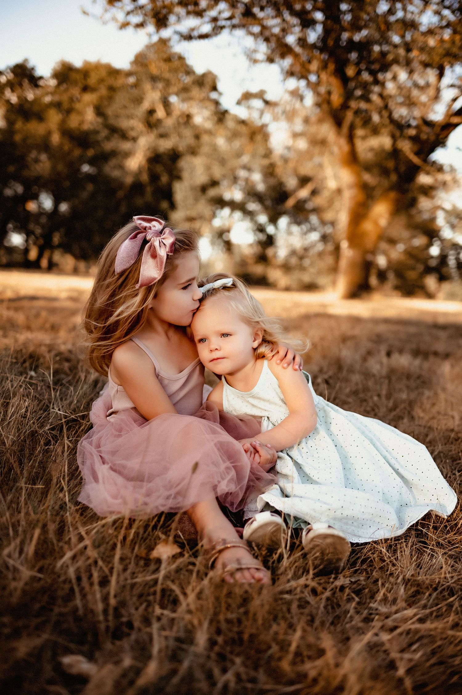 Two children in tulle dresses sharing tender moment in golden field.